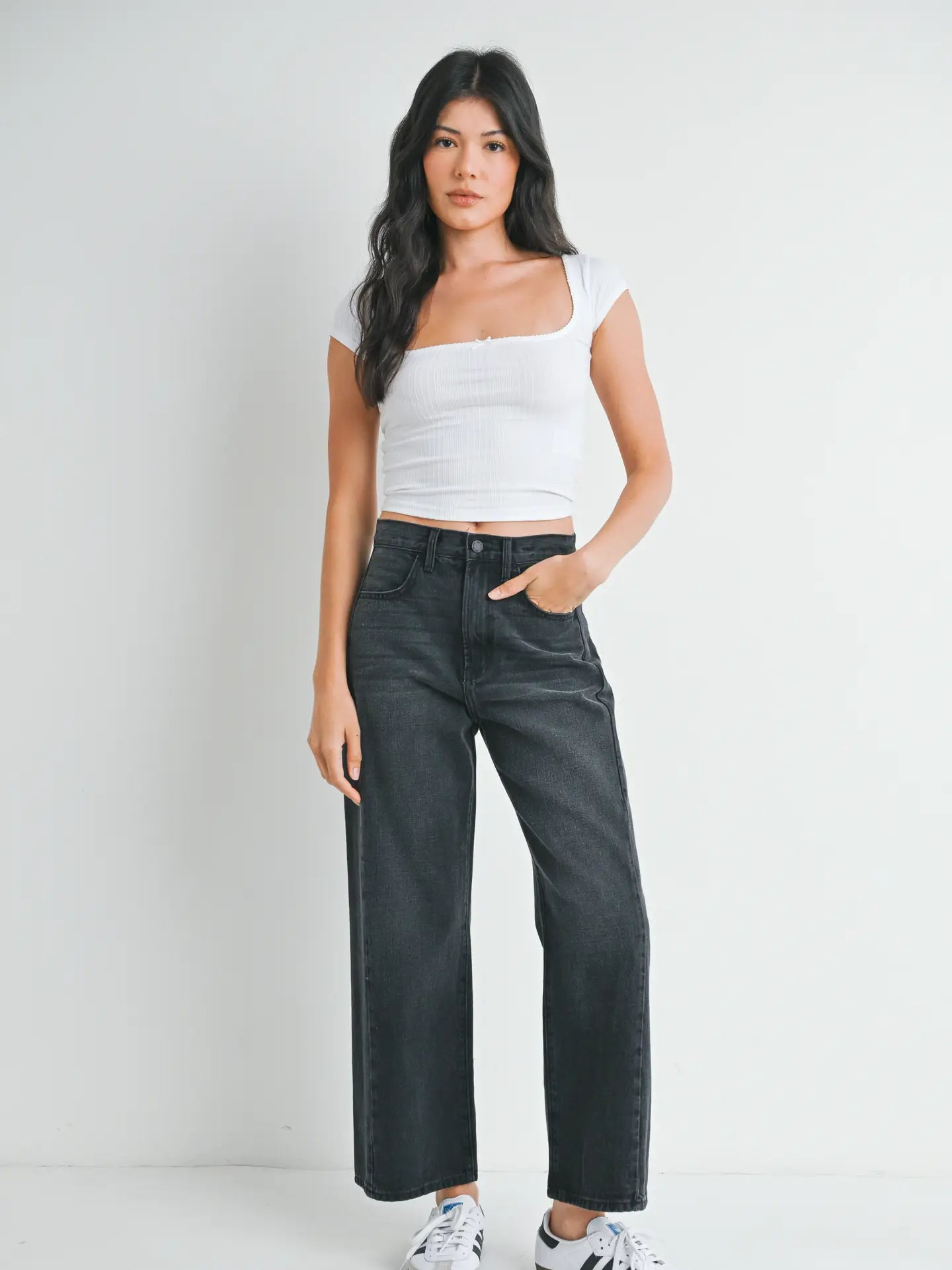 woman wearing black jeans and white top in front of a white background. 