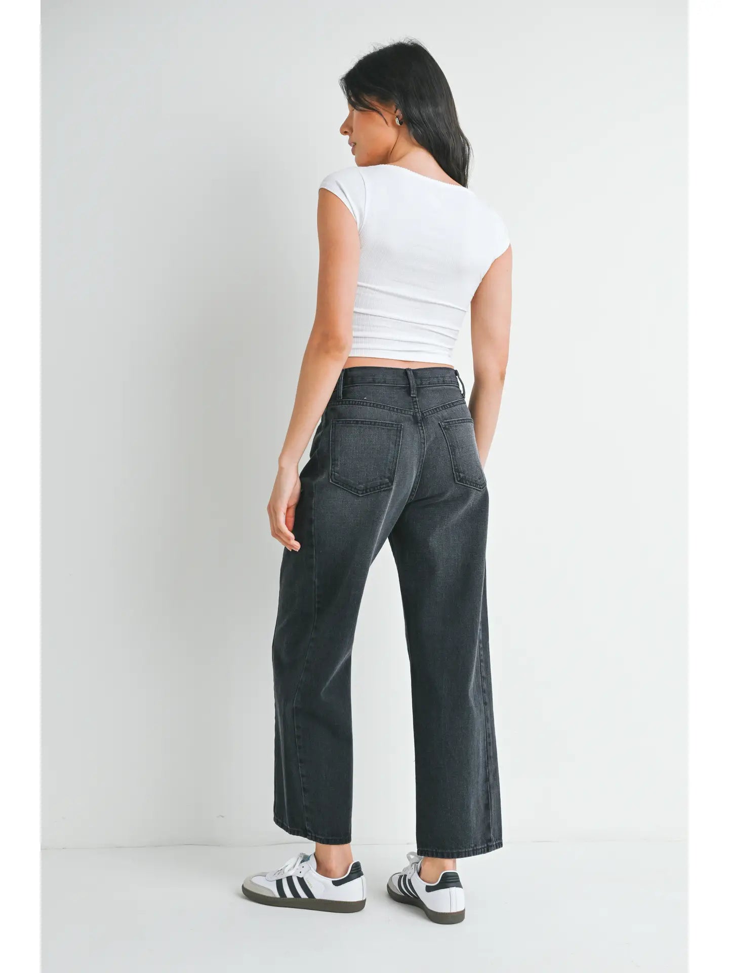 woman wearing black jeans and white top in front of a white background. 