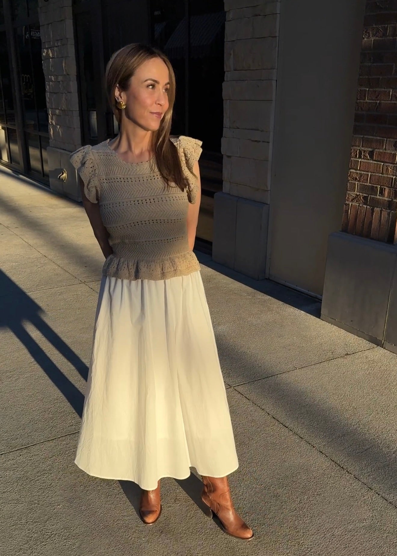 Woman wearing white dress with brown knit top with brown boots