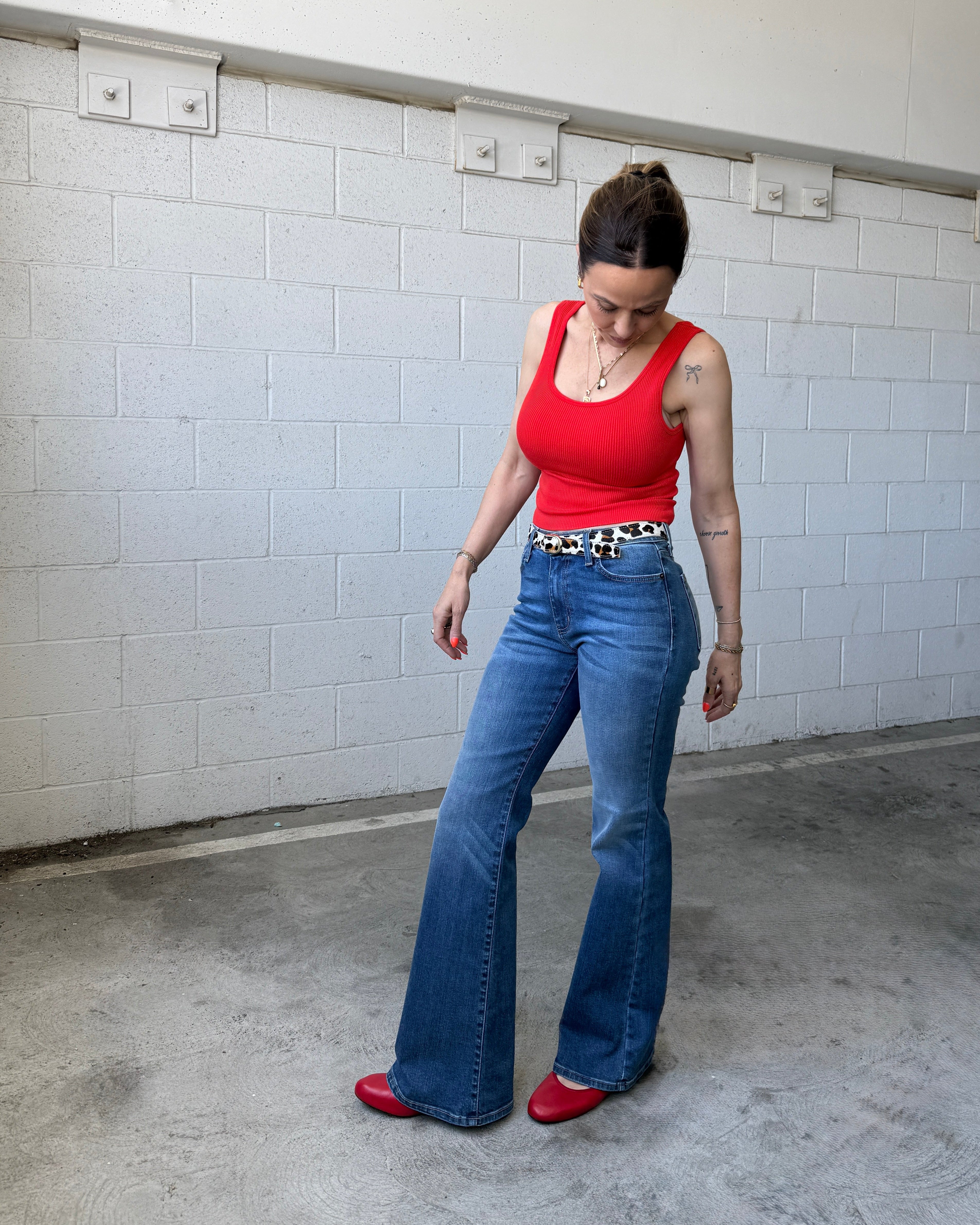 Woman wearing a red top and blue jeans standing in a tiled room.