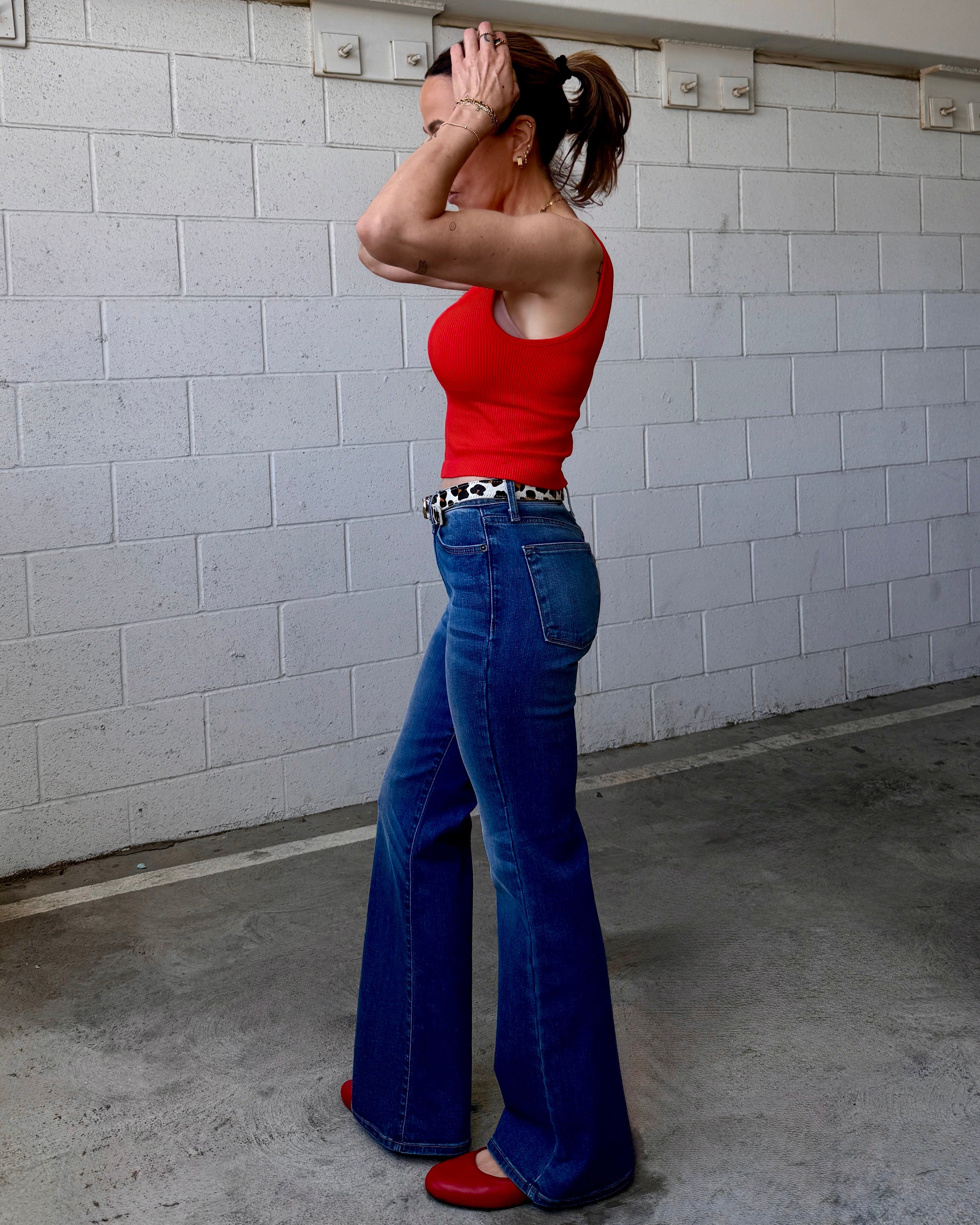 Woman in red top and blue jeans standing in a garage.