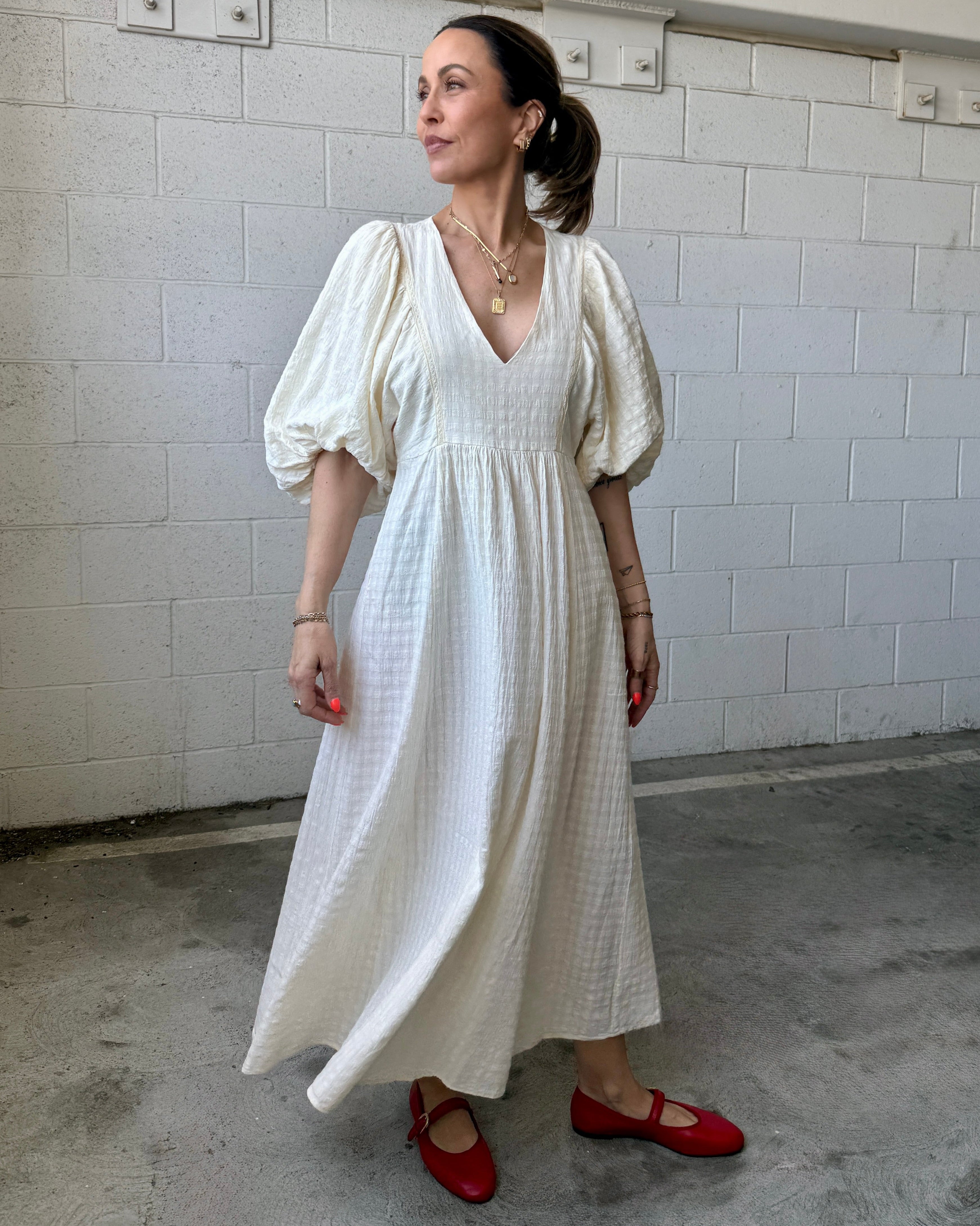 Woman in a white dress with puffed sleeves standing against a tiled wall.