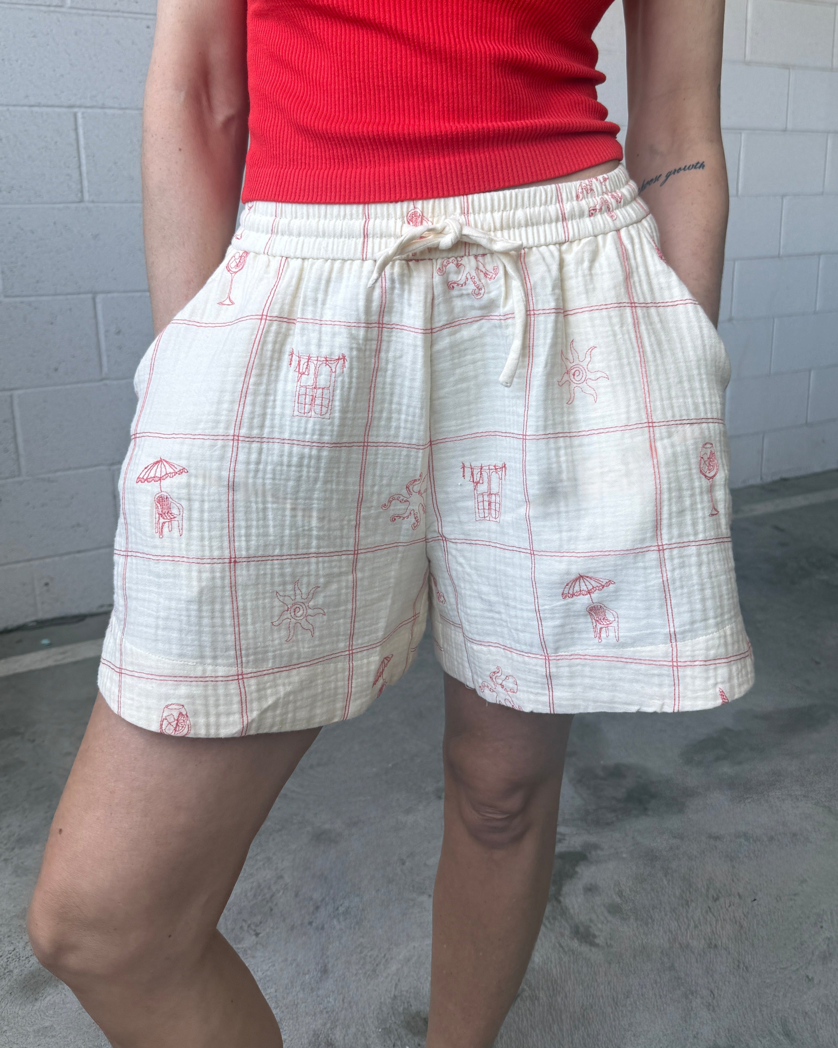 Person wearing a red top and white plaid shorts with red patterns against a gray tiled wall.