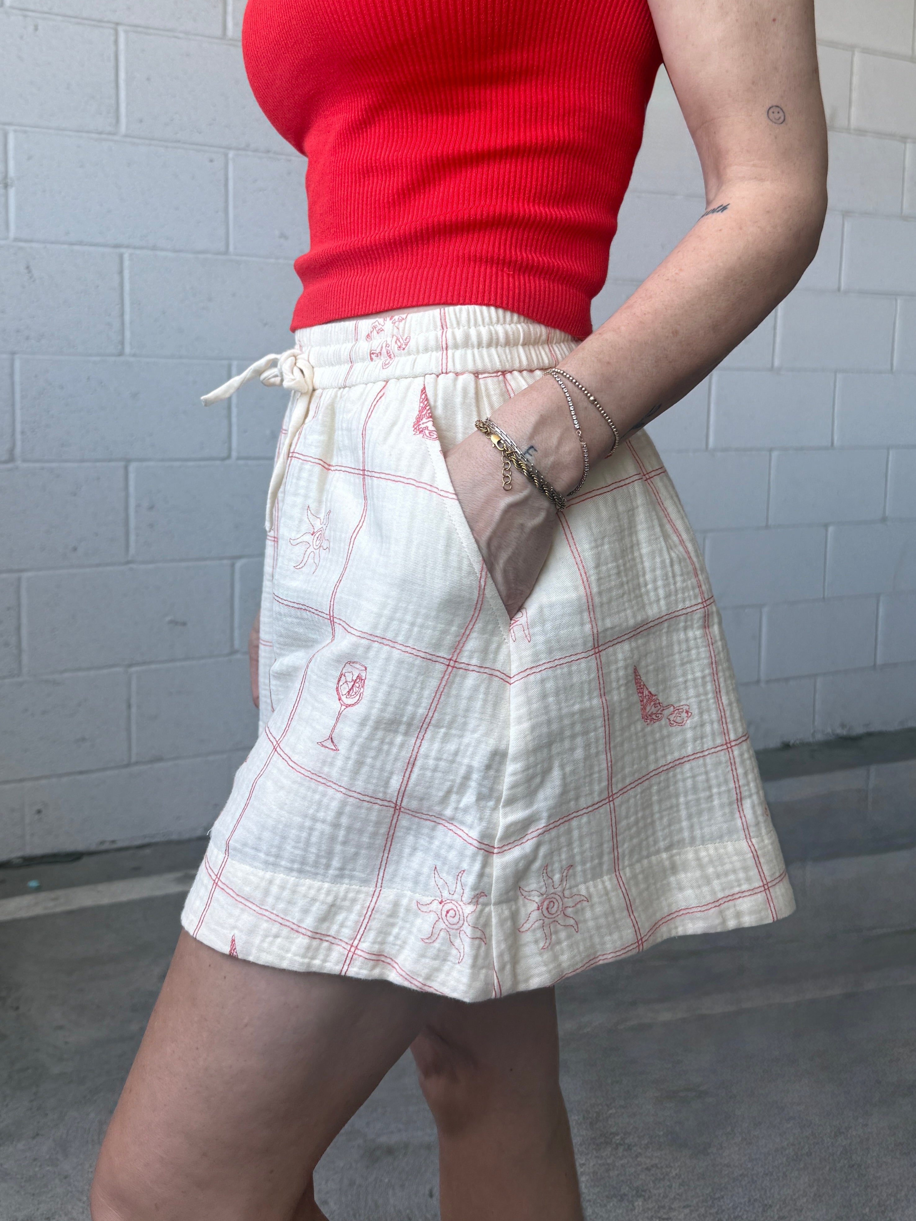 Person wearing a red top and white plaid skirt against a gray tiled wall.