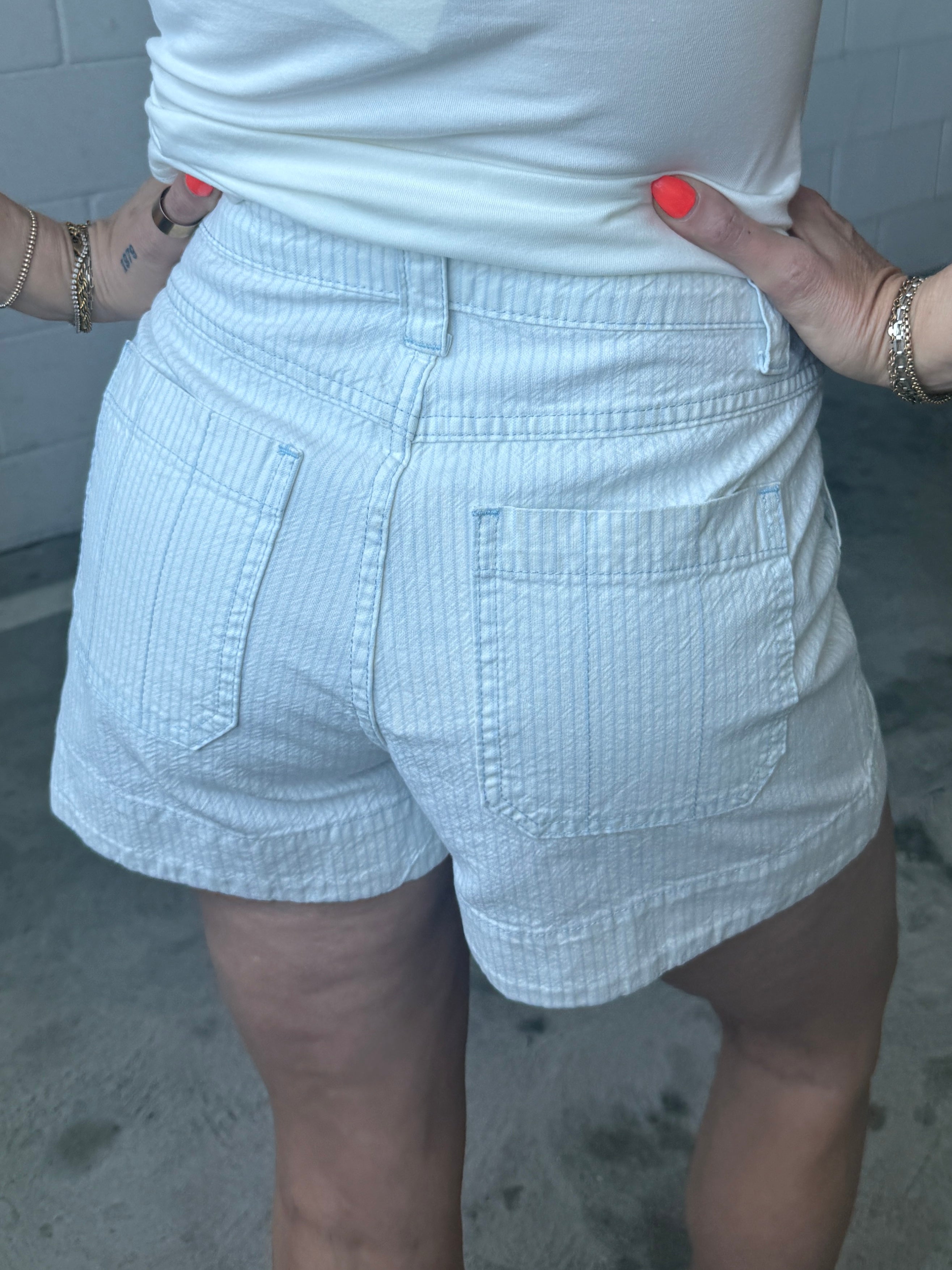 Person wearing light blue shorts and a white top with a neutral background