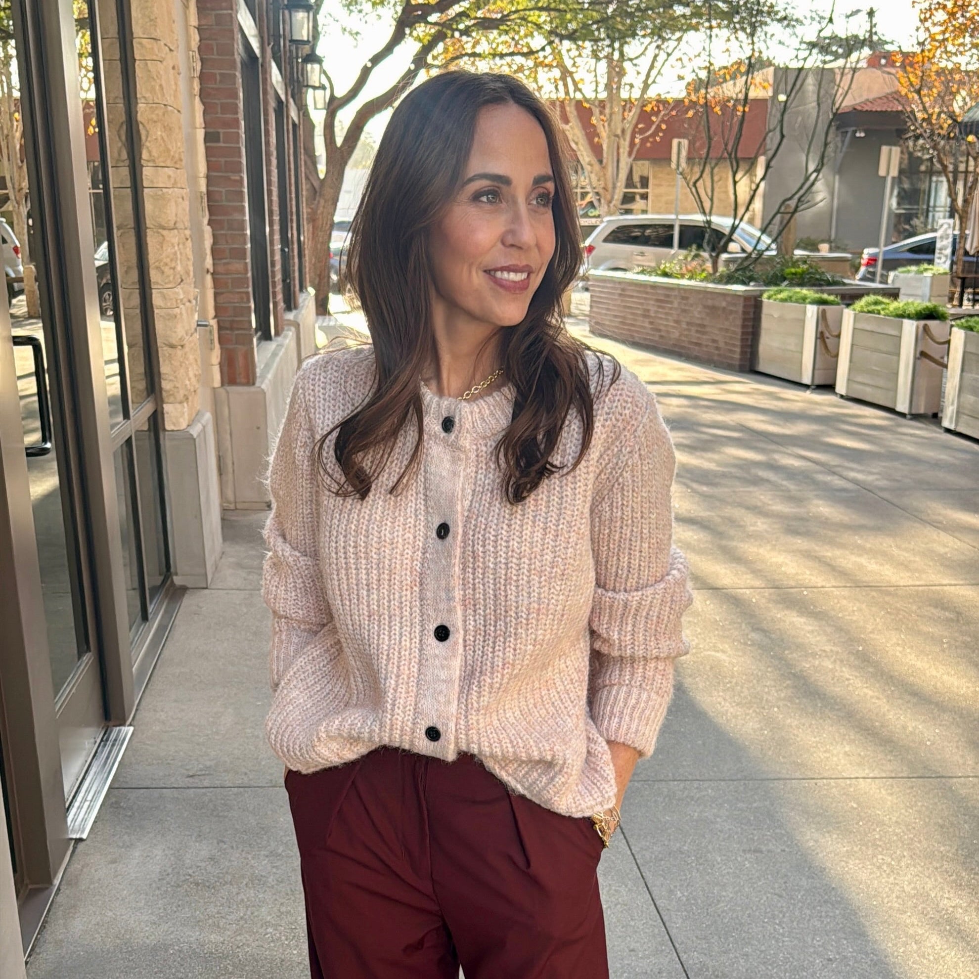 model wearing beautiful light rose colored cardigan and red pleated pants 