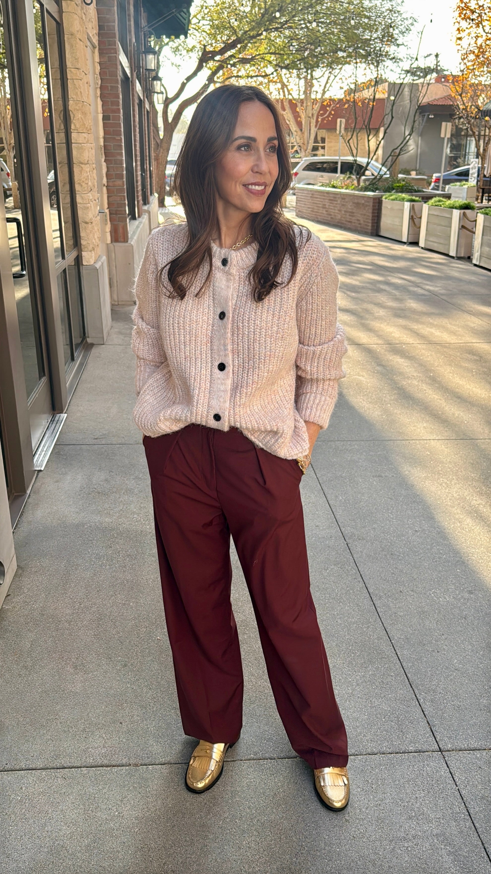 model wearing beautiful light rose colored sweater cardigan and red pleated pants 