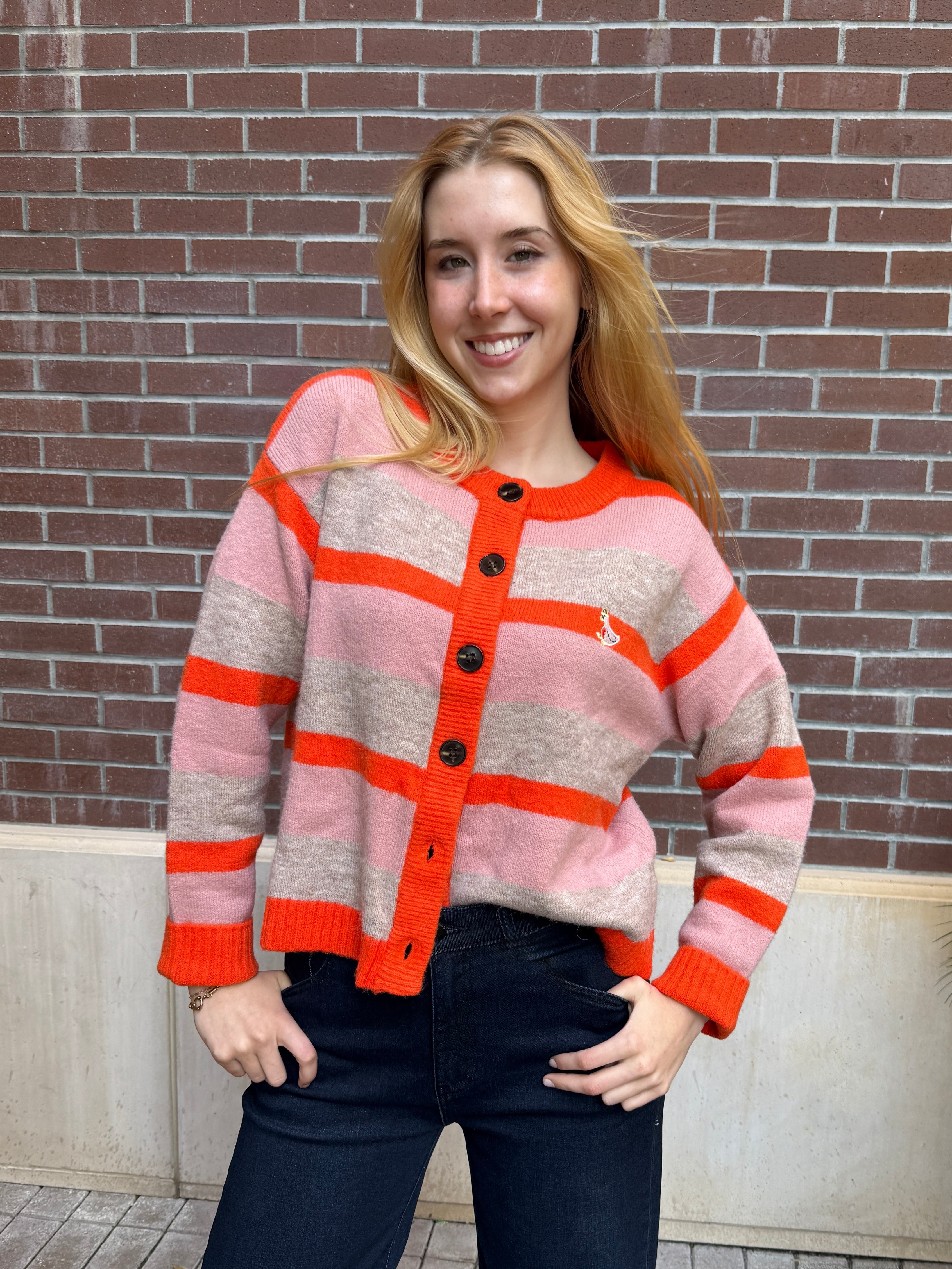 Woman wearing a pink and orange cardigan standing in front of a brick wall.