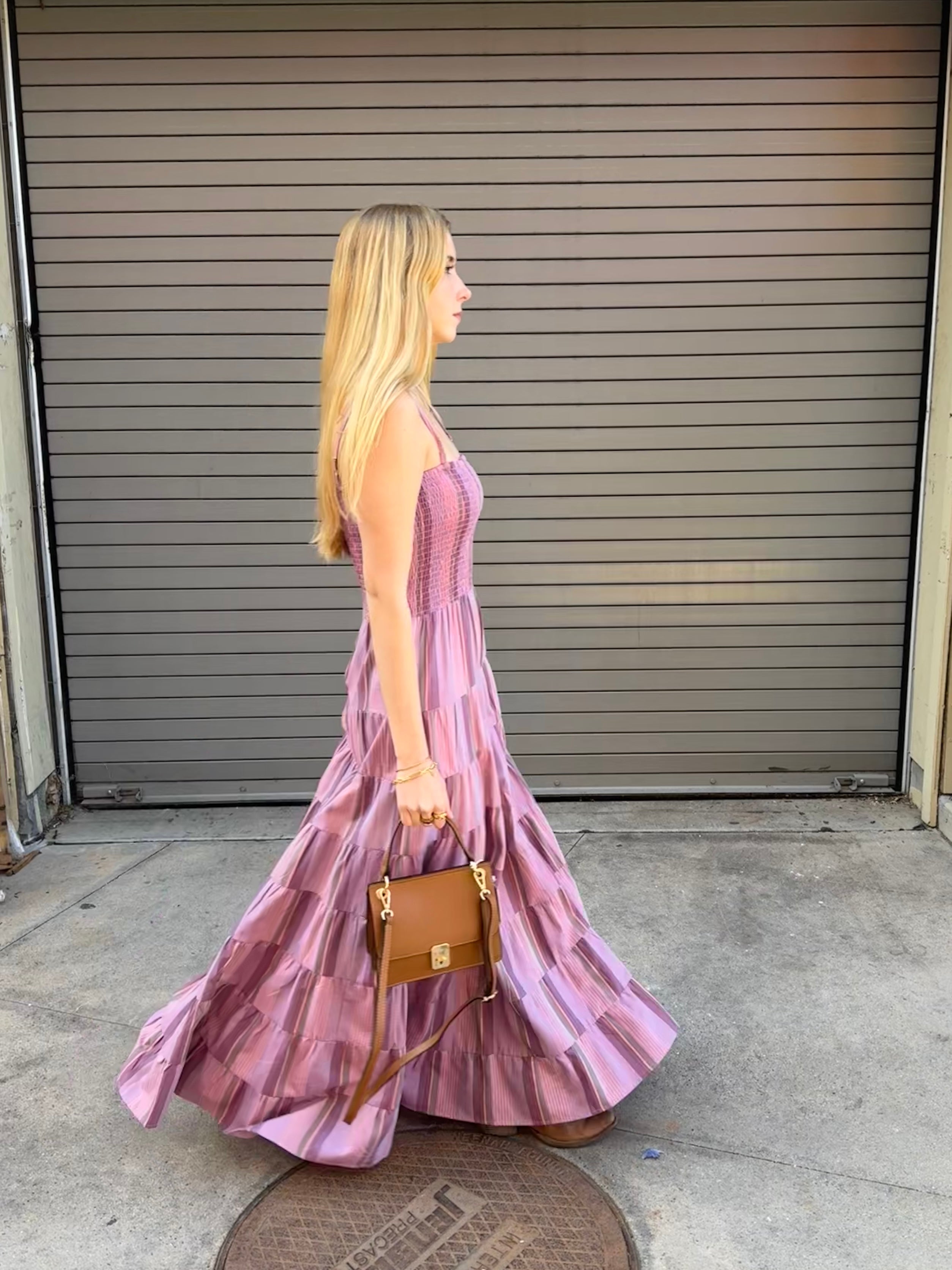 Woman in a pink dress holding a brown handbag in front of a closed garage door.