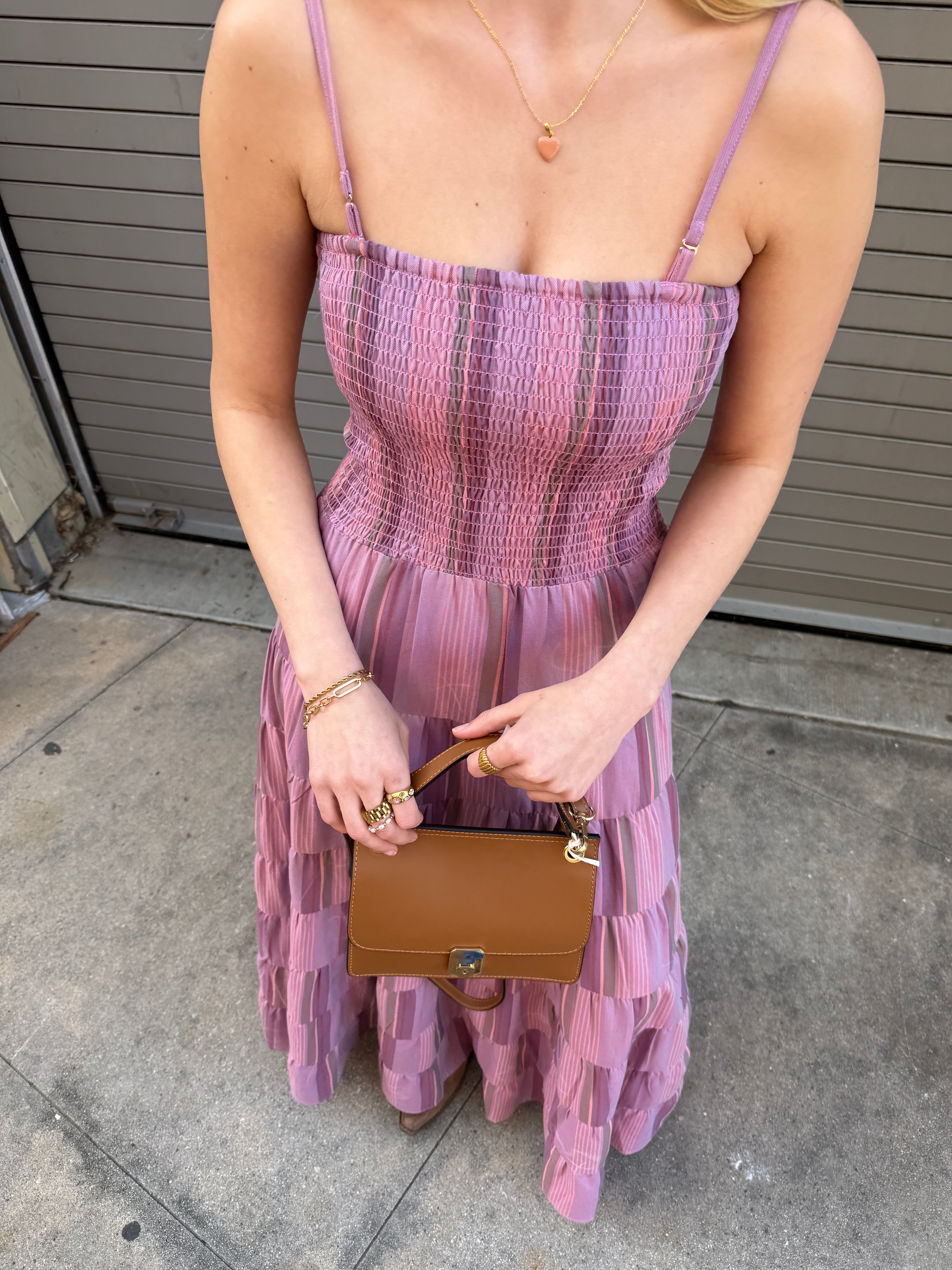 Woman in a pink dress holding a brown handbag on a concrete floor.