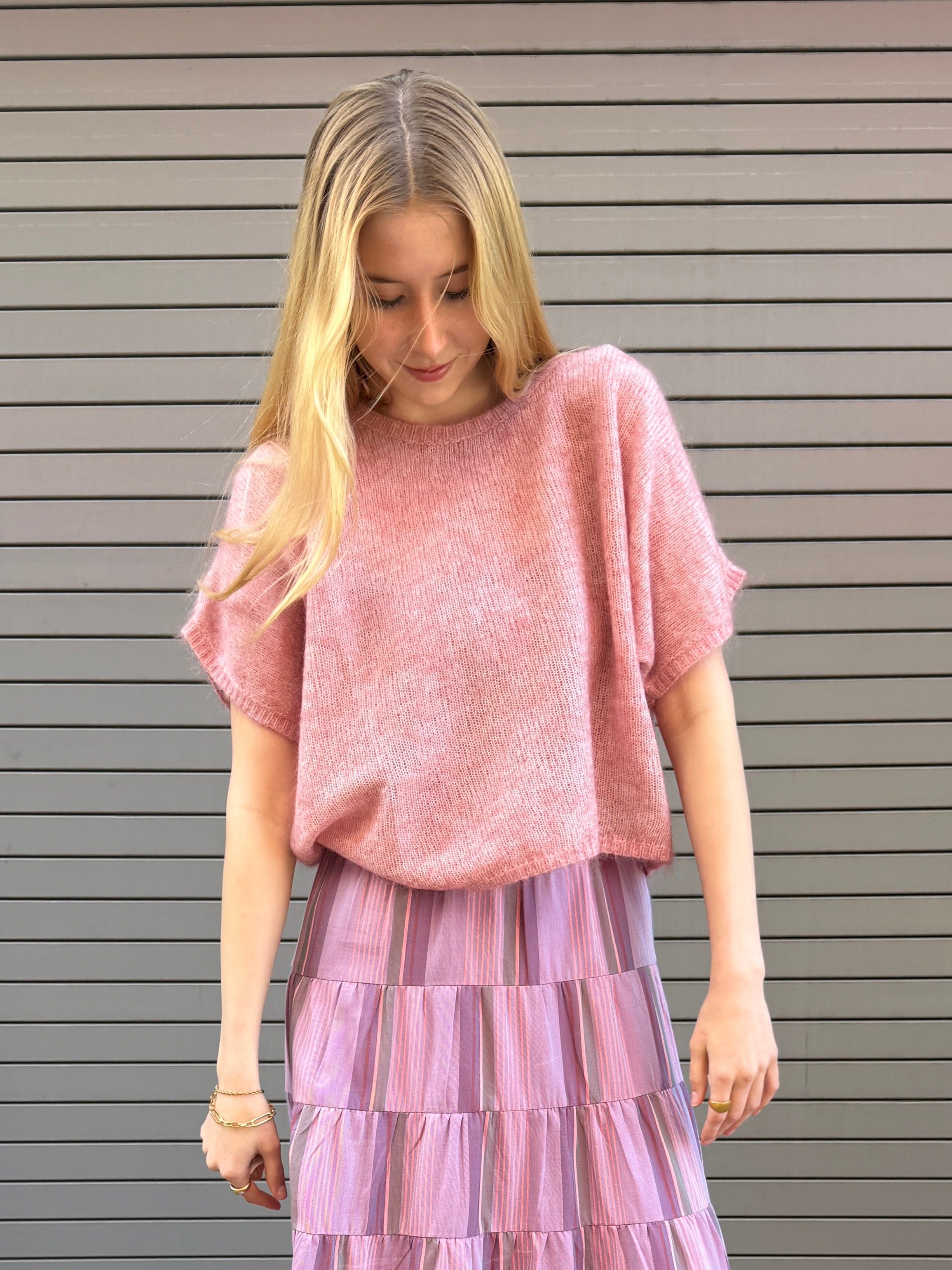 Woman wearing a pink top and purple skirt against a gray background