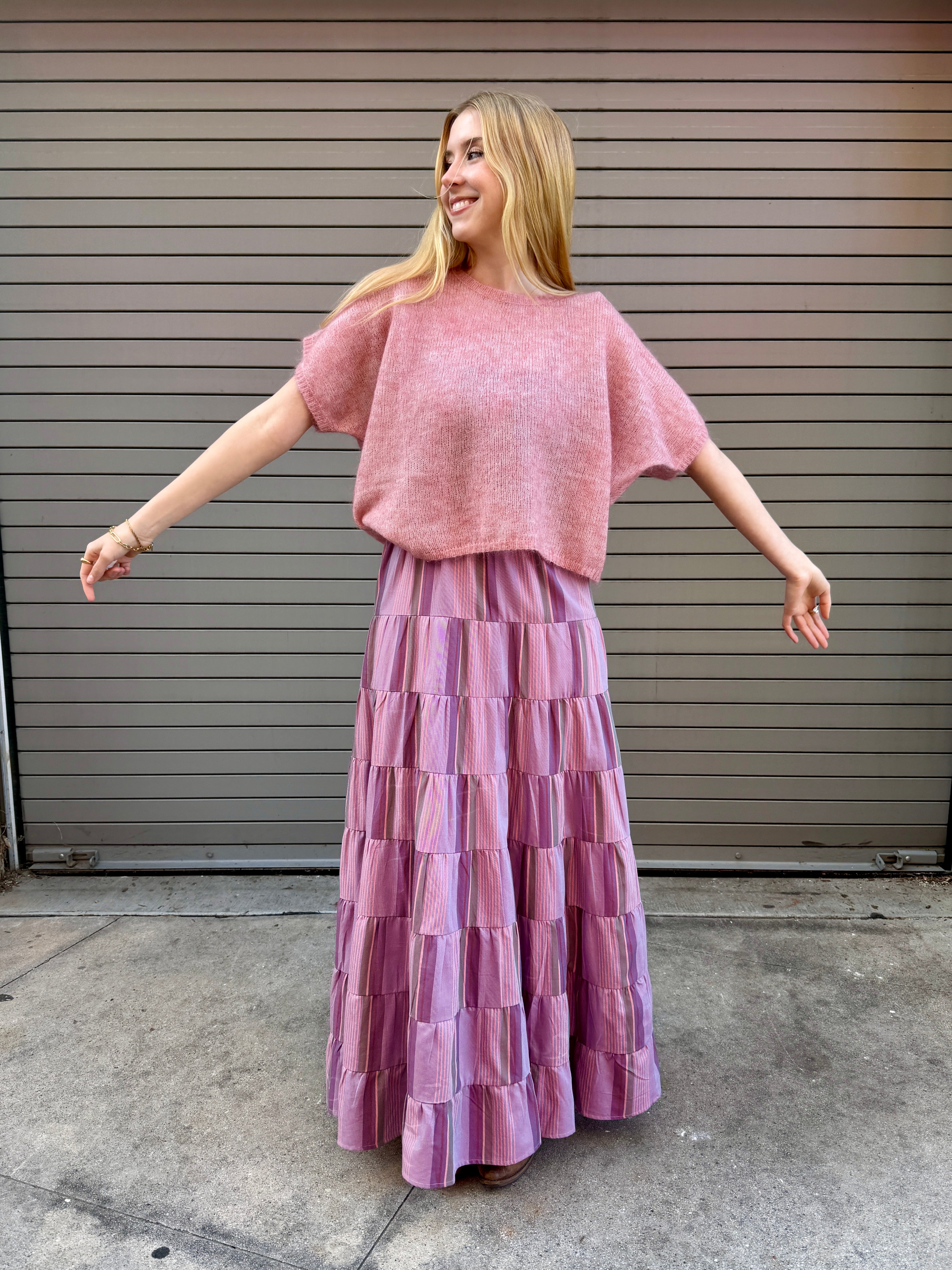 Woman wearing a pink outfit with a layered skirt in front of a metallic shutter.