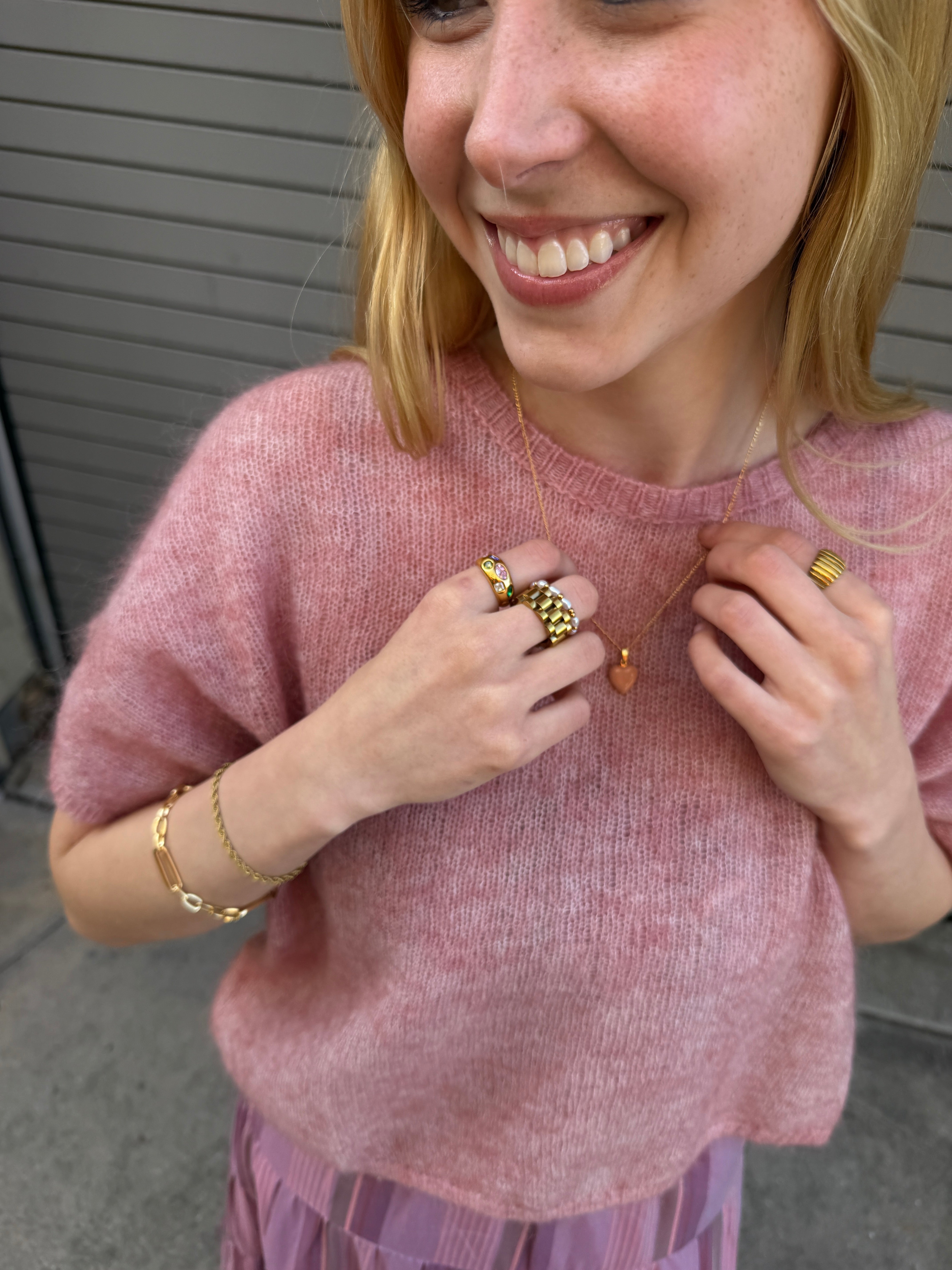 Woman wearing multiple rings and a bracelet on a pink sweater.