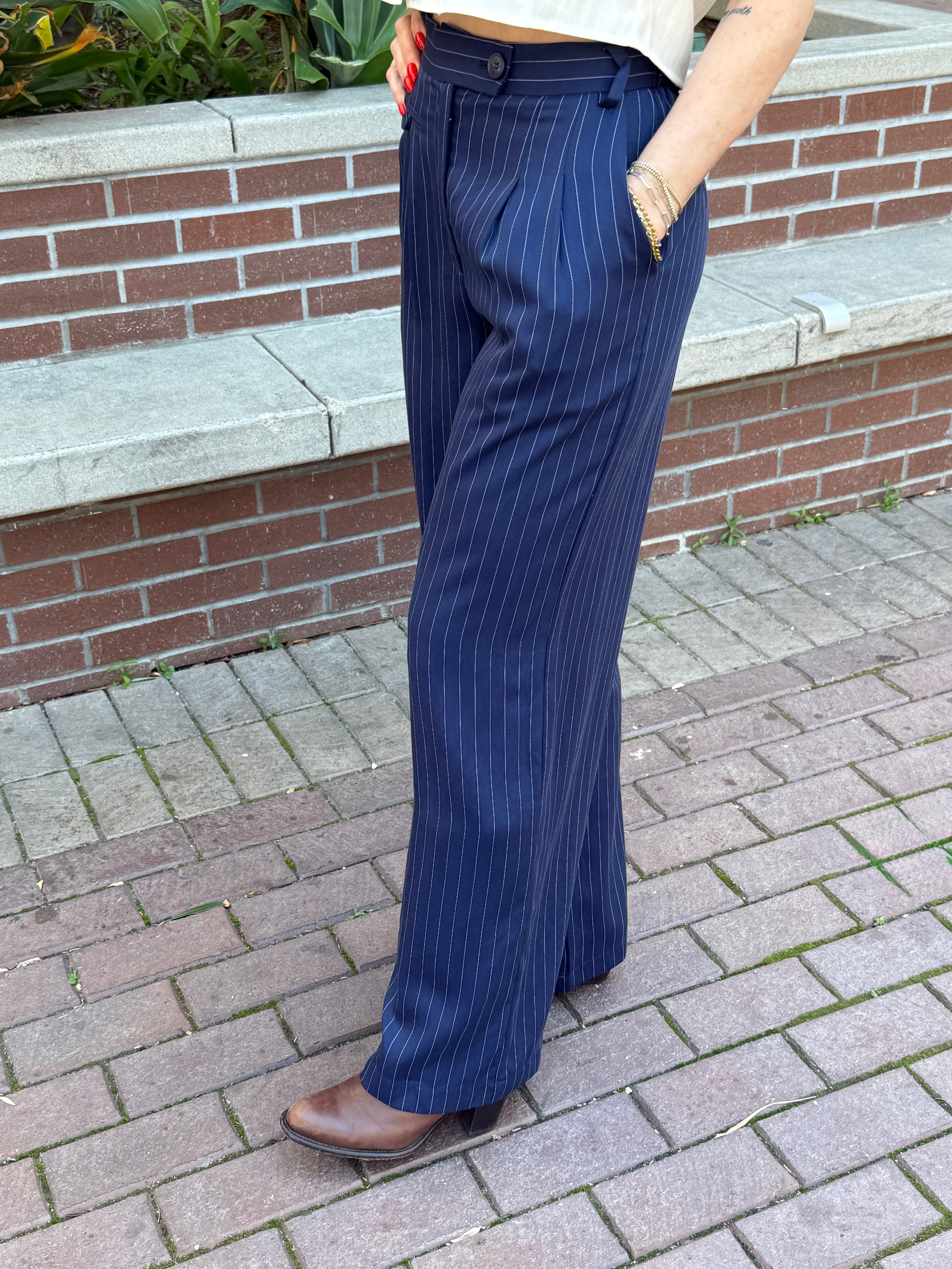 Person wearing blue pinstripe pants standing on a brick pavement.