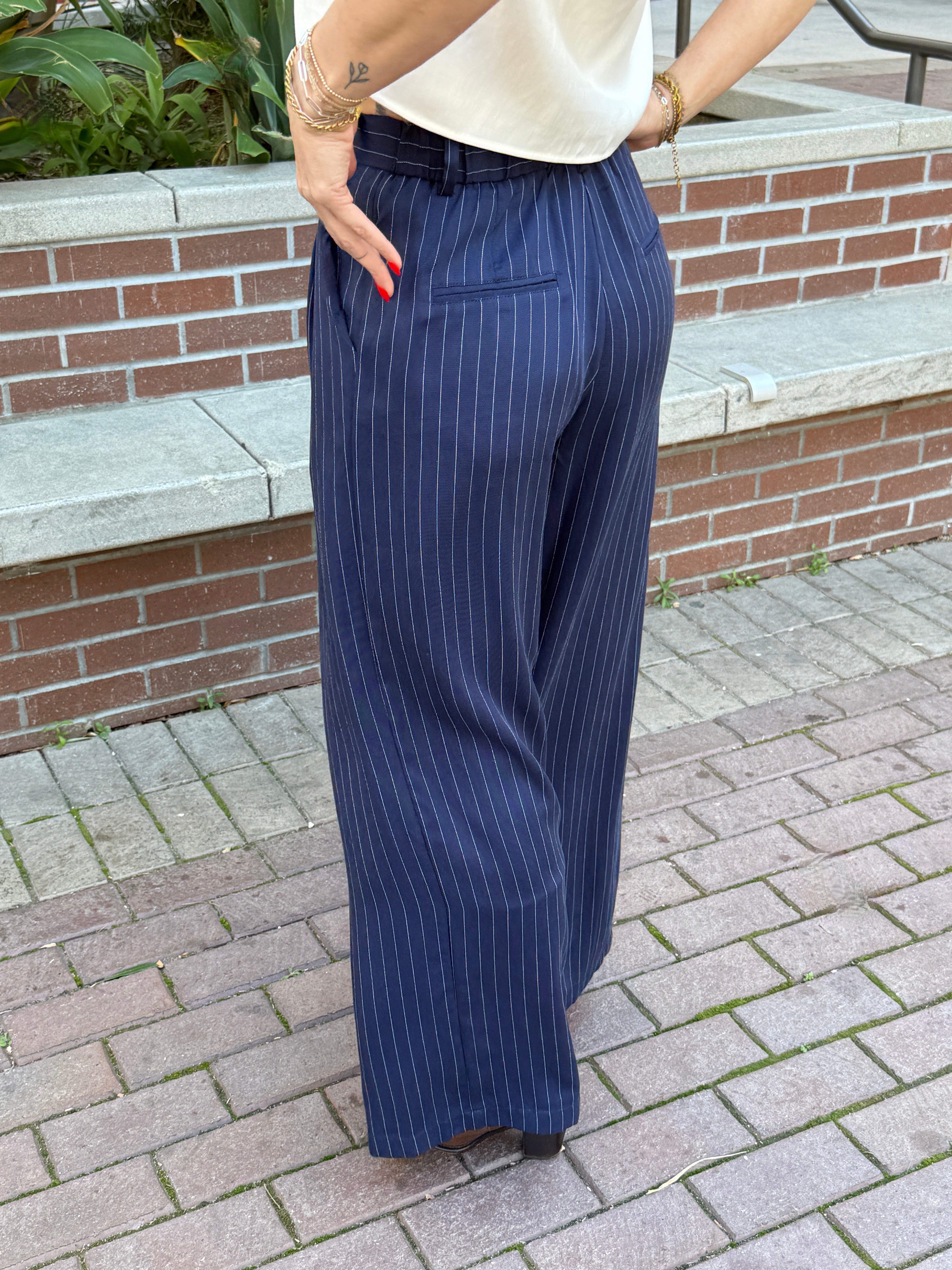Person wearing blue pinstripe pants standing on a paved area with a brick wall in the background.