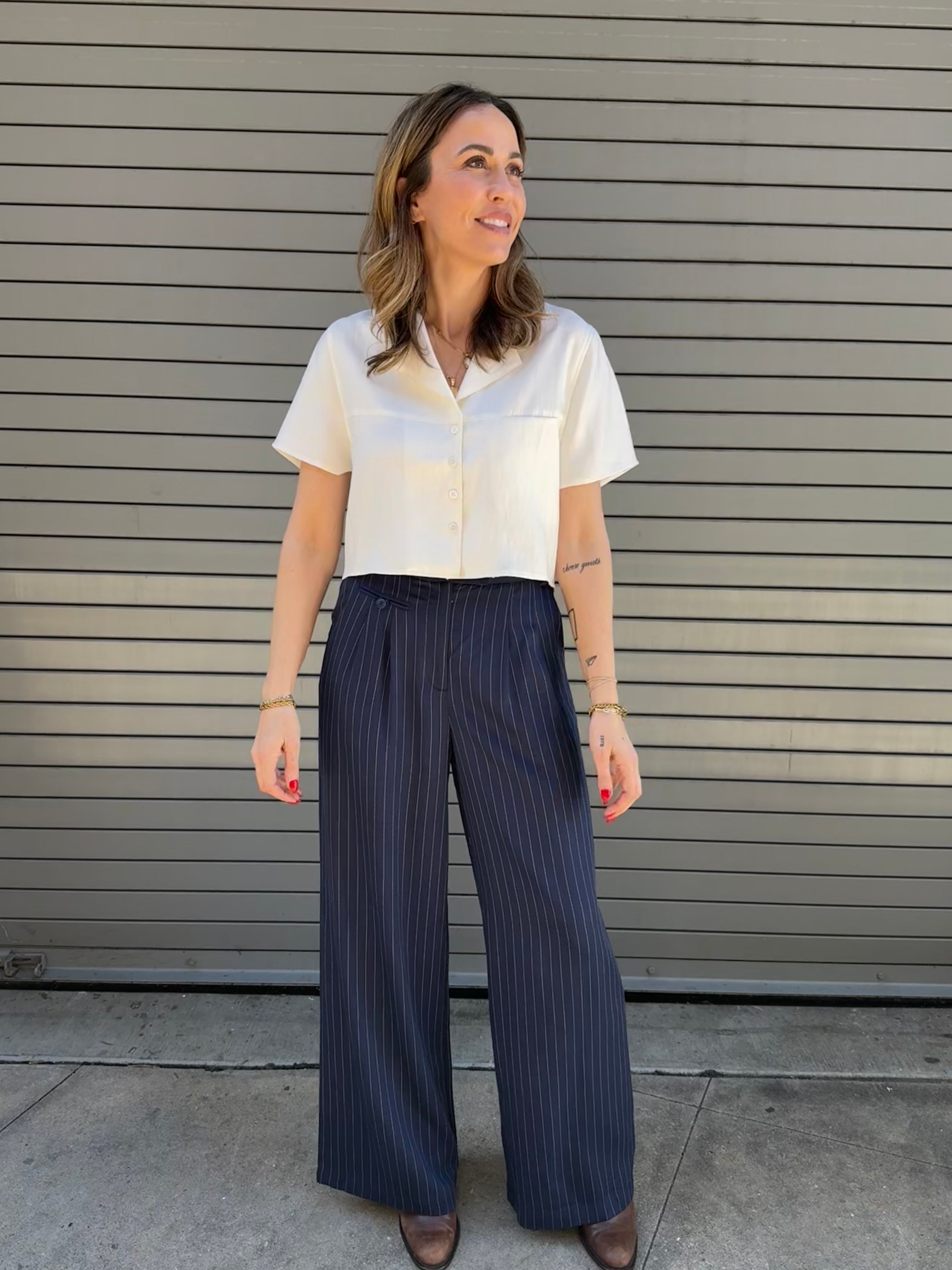 Woman wearing a white blouse and navy striped pants standing against a metallic shutter.