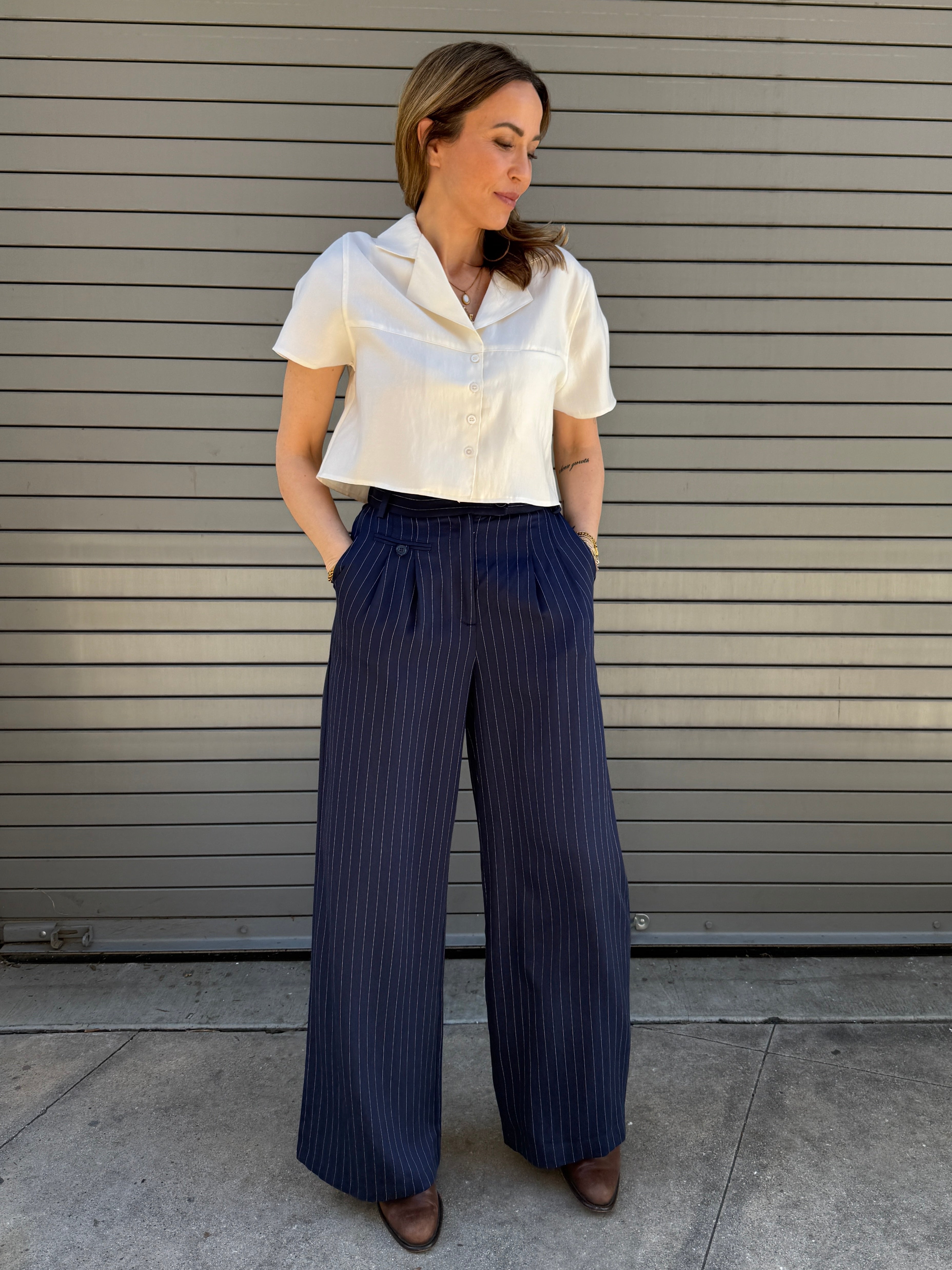 Woman wearing a white blouse and navy pinstripe pants standing against a gray wall.