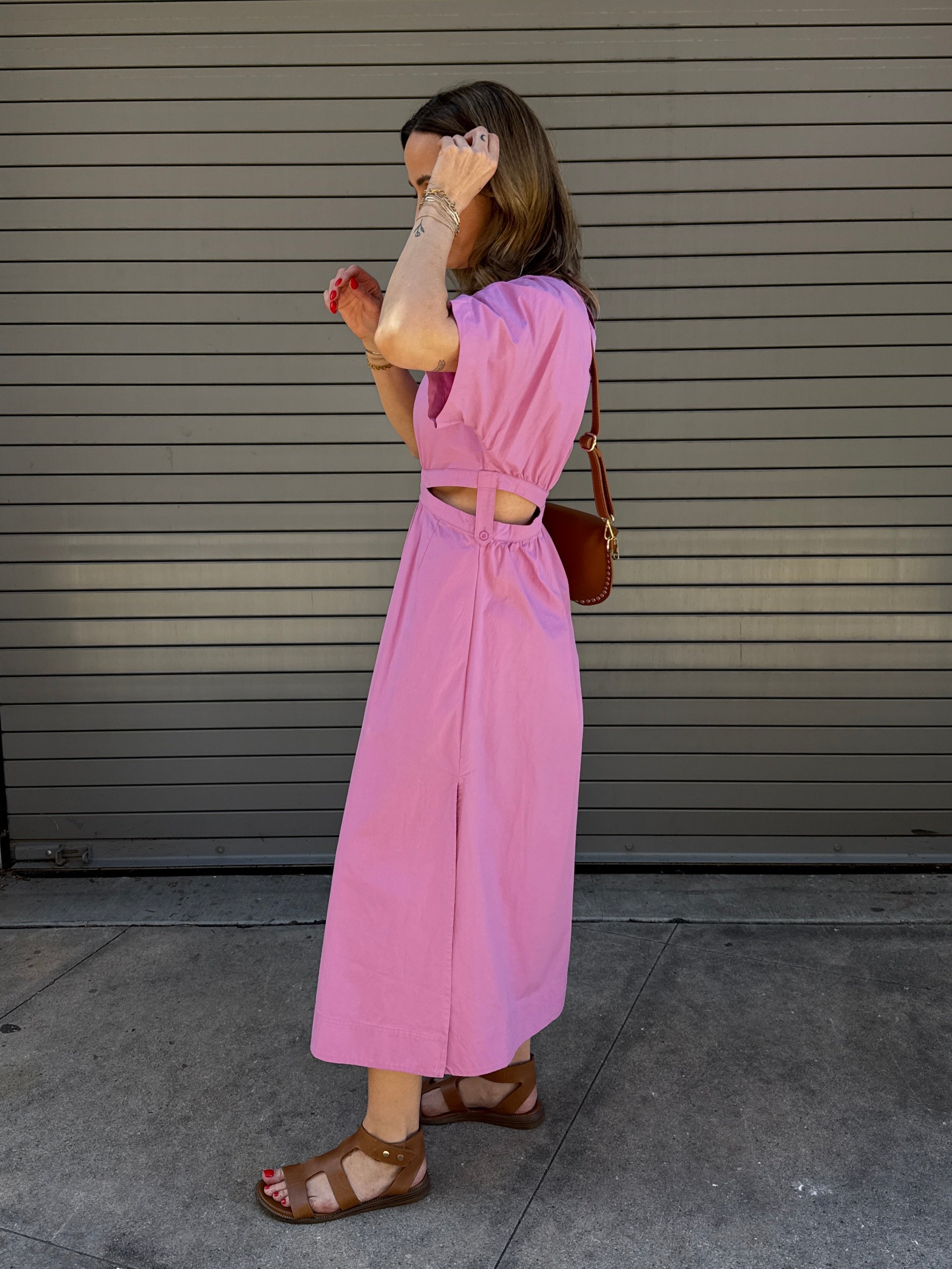 Woman wearing a pink outfit standing against a gray wall.