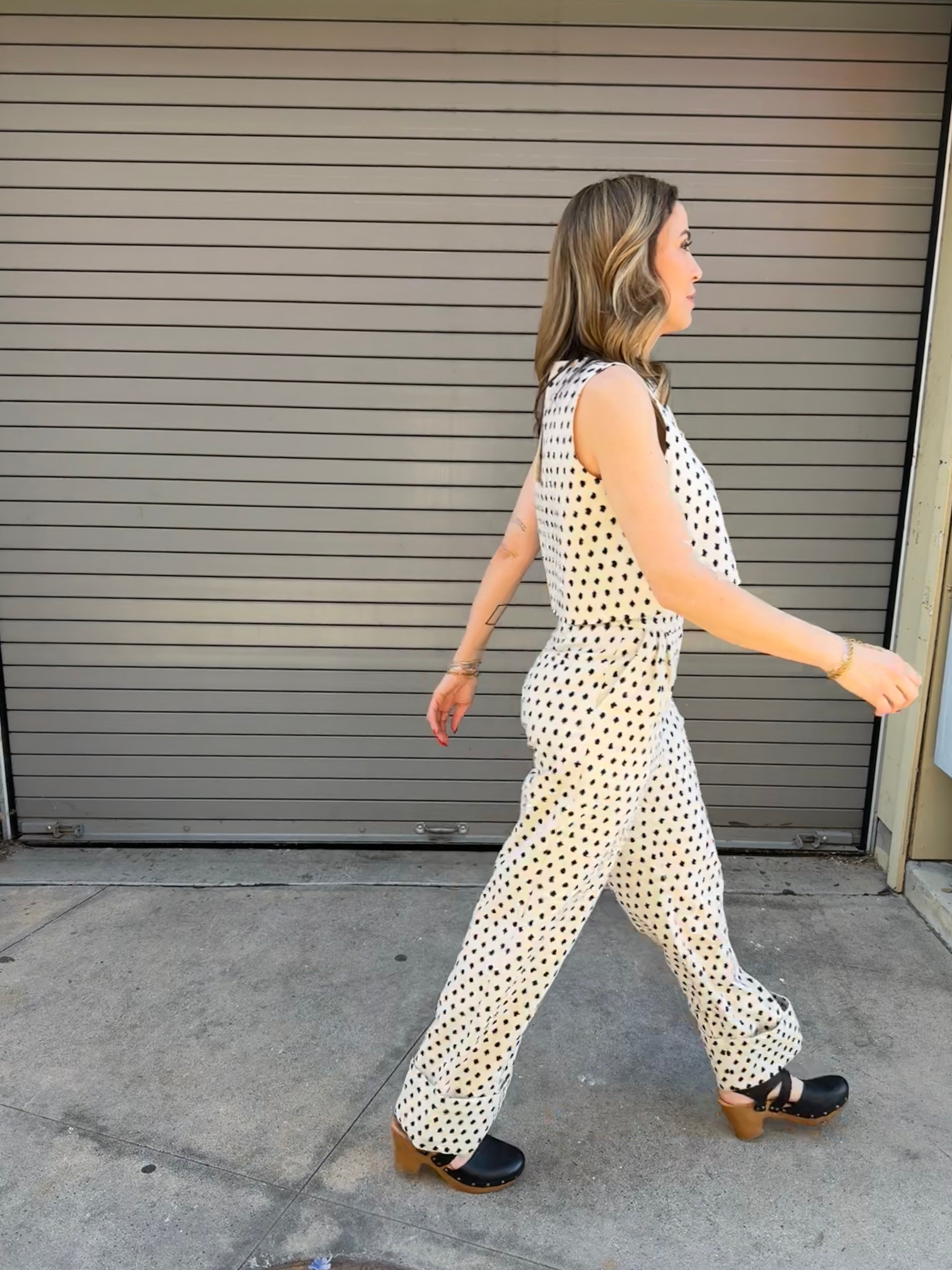 Woman in a polka dot jumpsuit walking past a closed garage door.