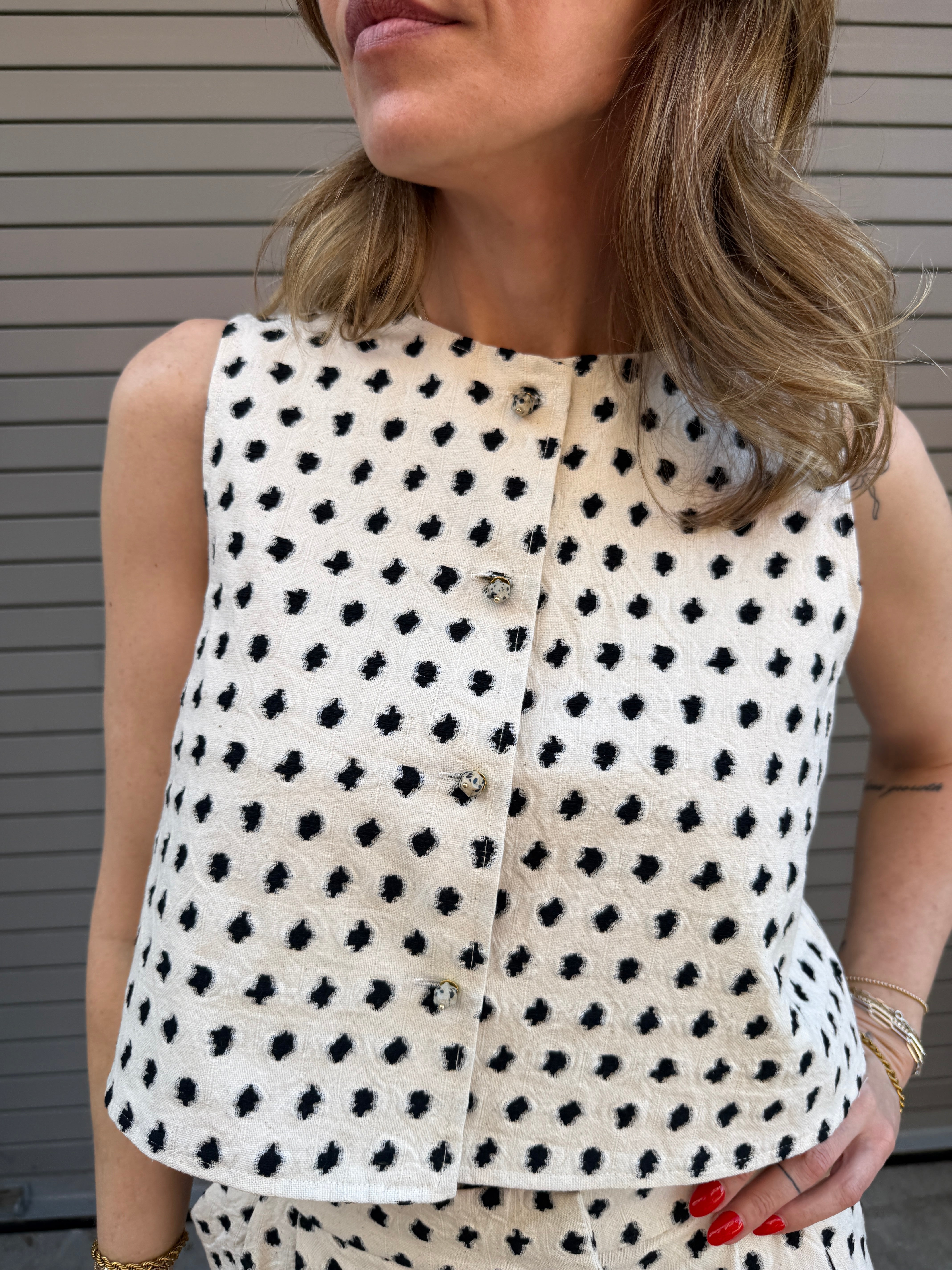Woman wearing a white sleeveless top with black polka dot pattern.