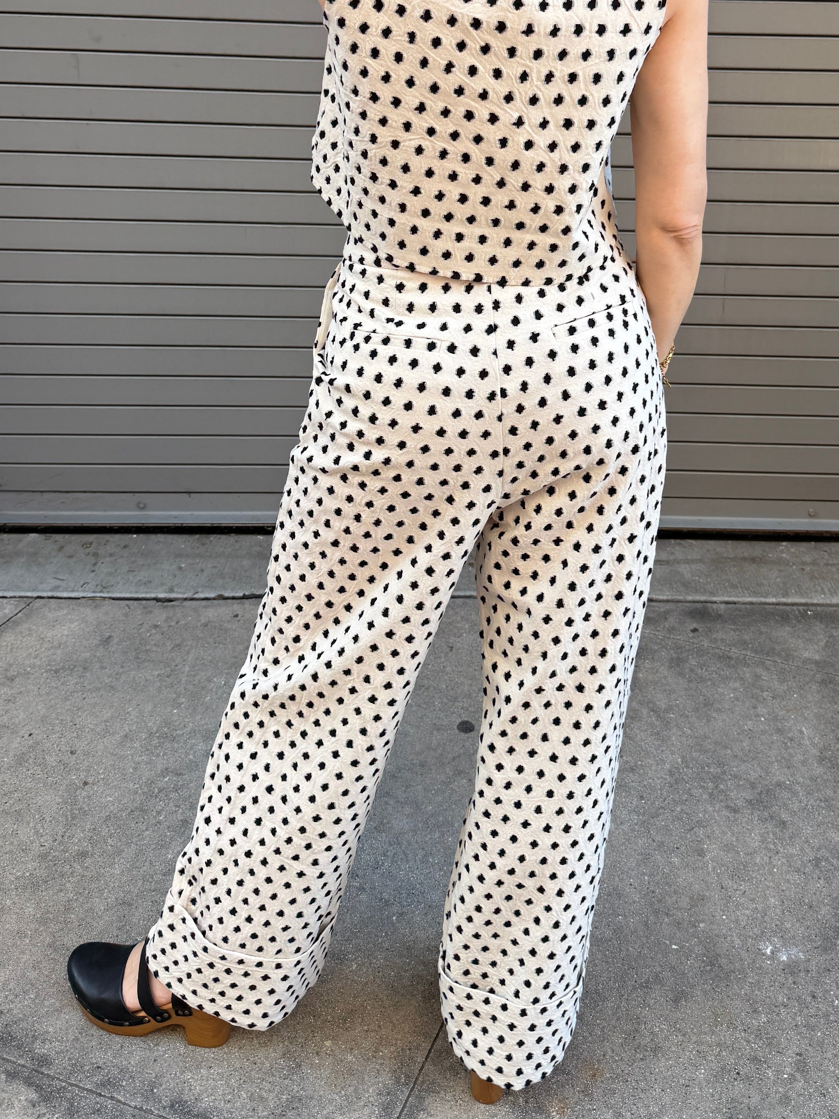 Person wearing a polka dot vest and pants standing in front of a metallic shutter.