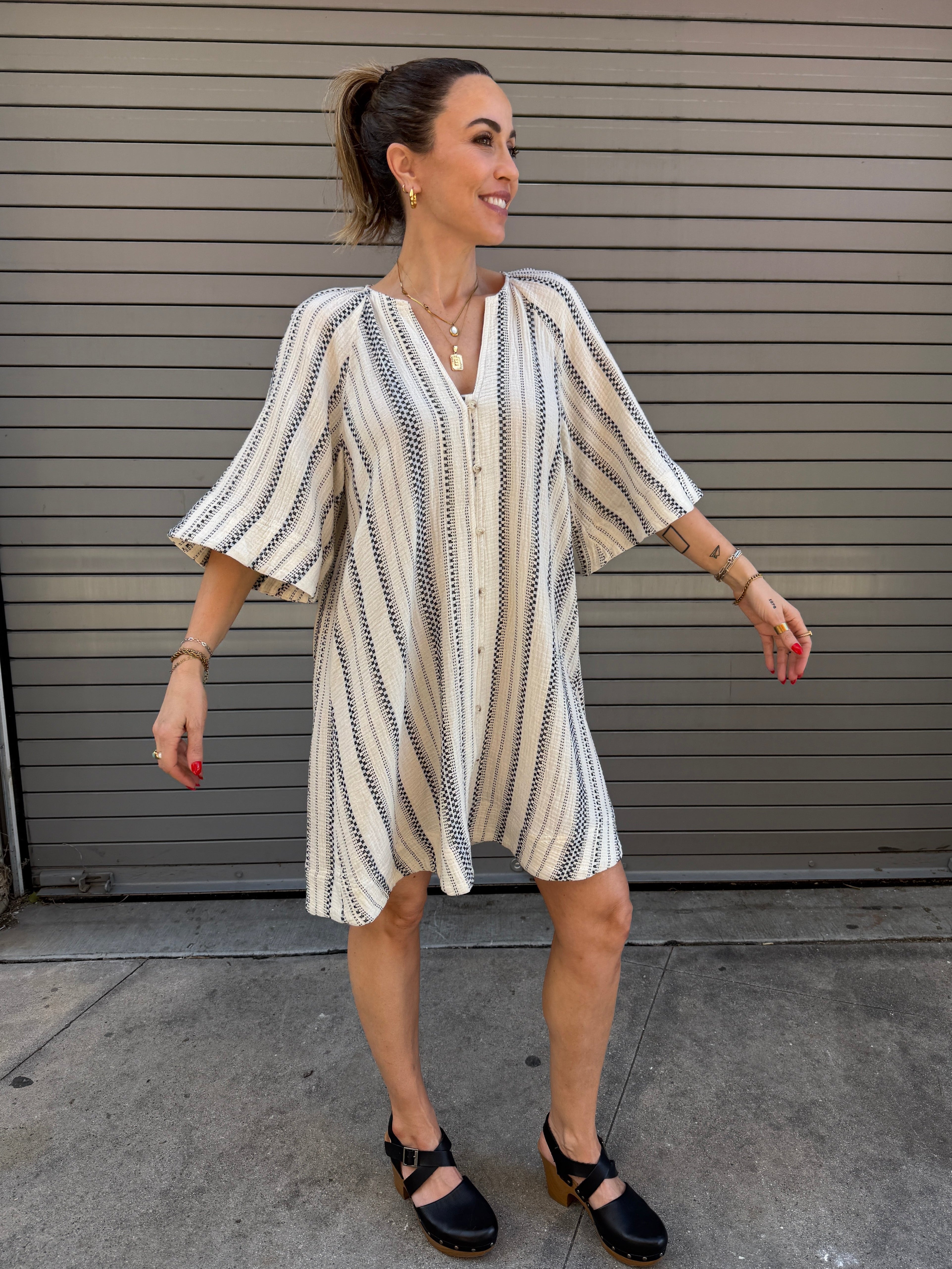 Woman wearing a striped dress standing in front of a metallic shutter.