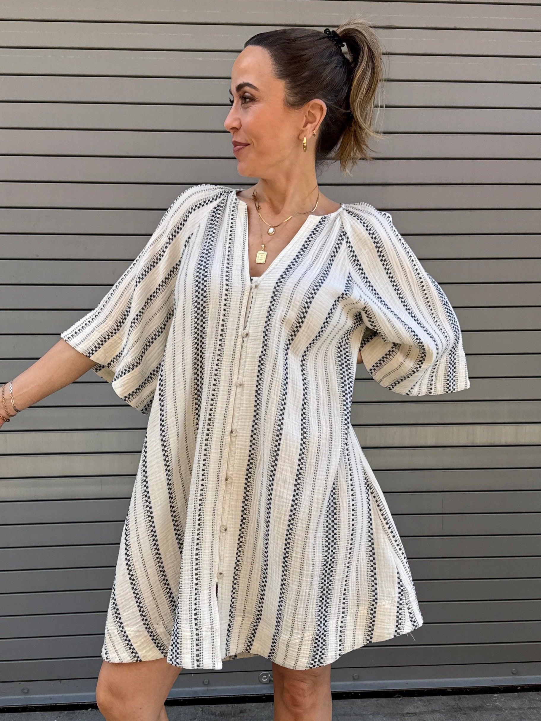 Woman in a striped dress standing on a concrete floor with a metal gate in the background