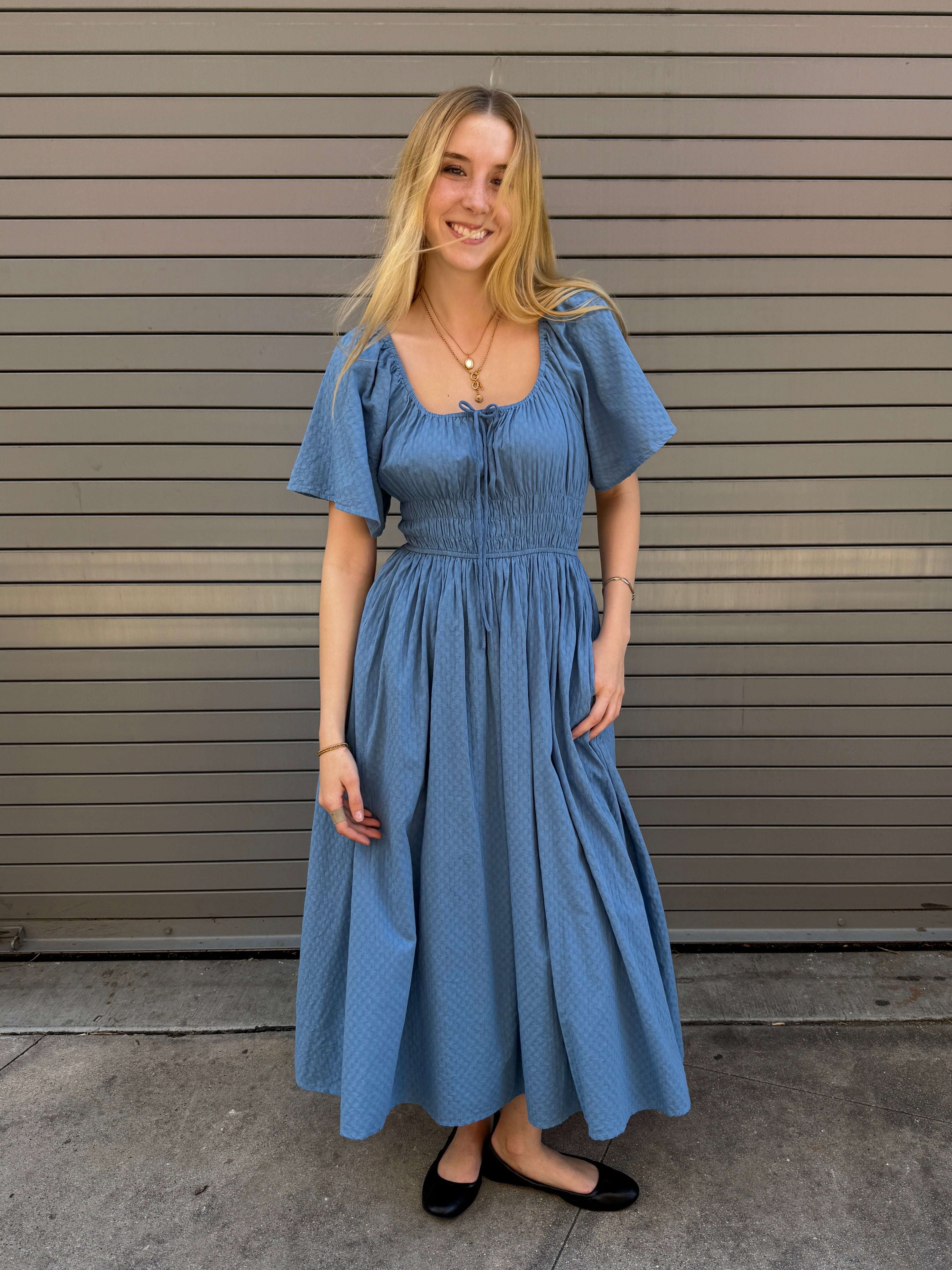 Woman wearing a blue dress standing in front of a metallic wall.