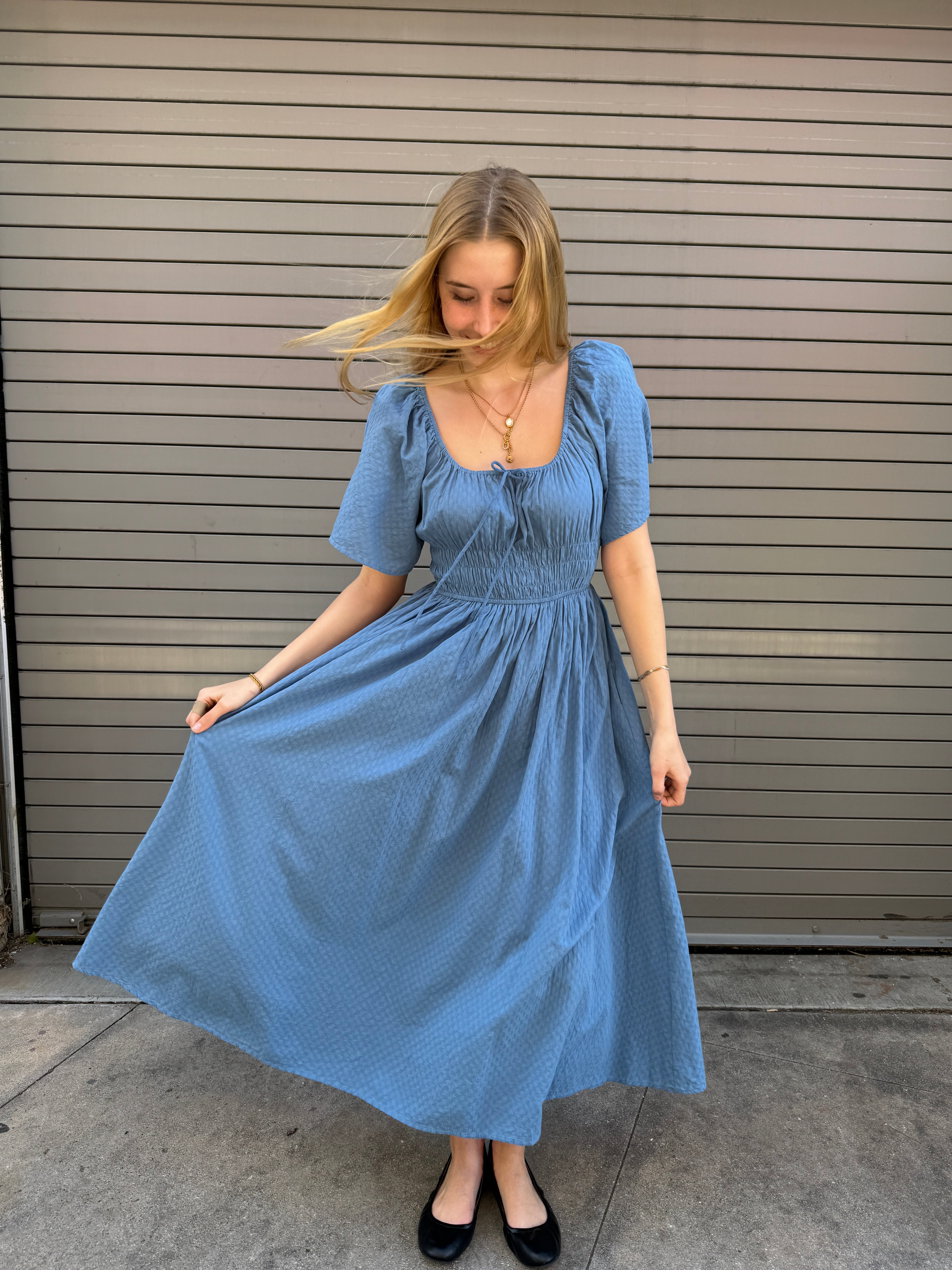 Woman wearing a blue dress standing on a concrete floor.