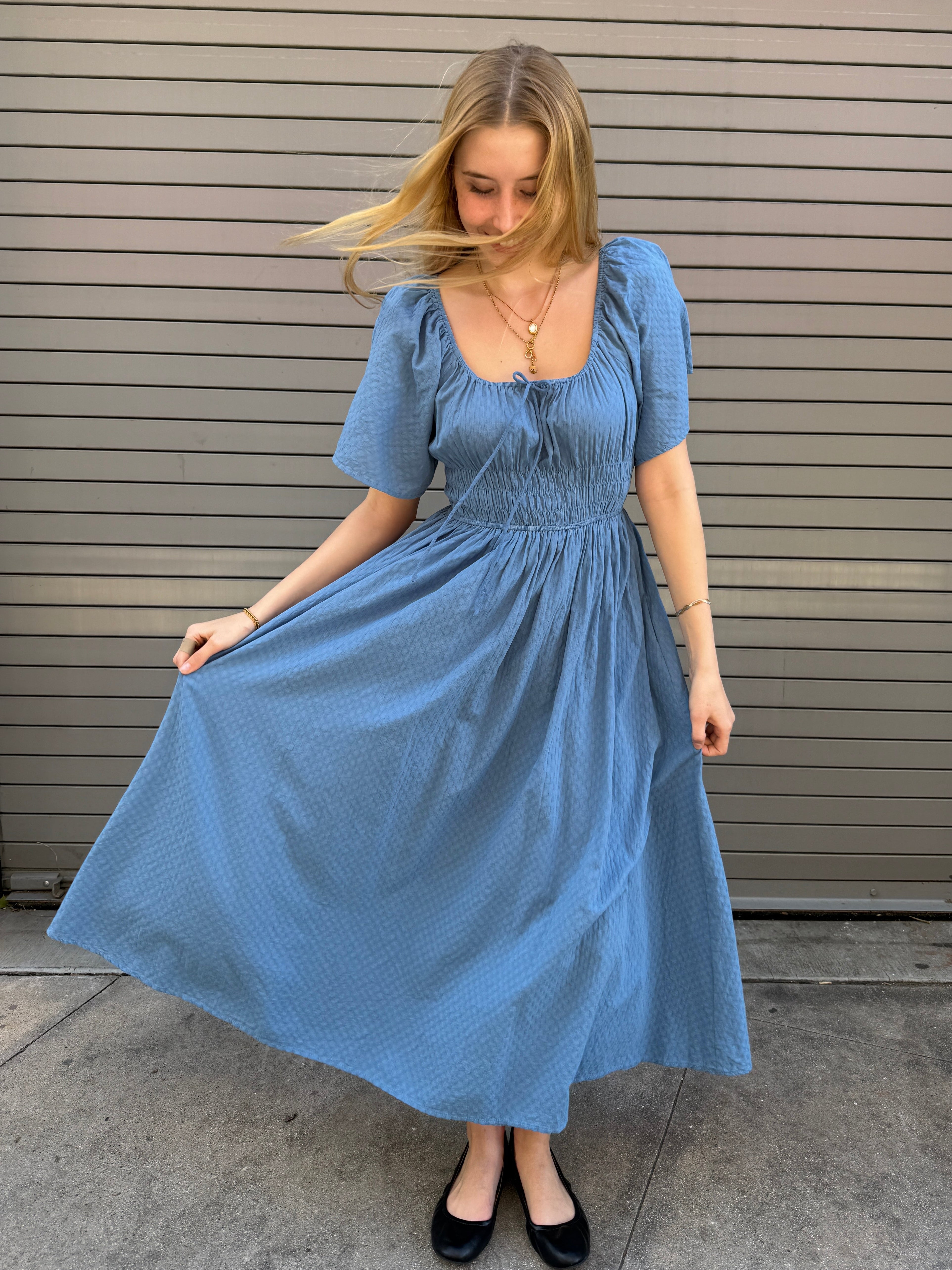 Woman wearing a blue dress standing on a concrete floor.