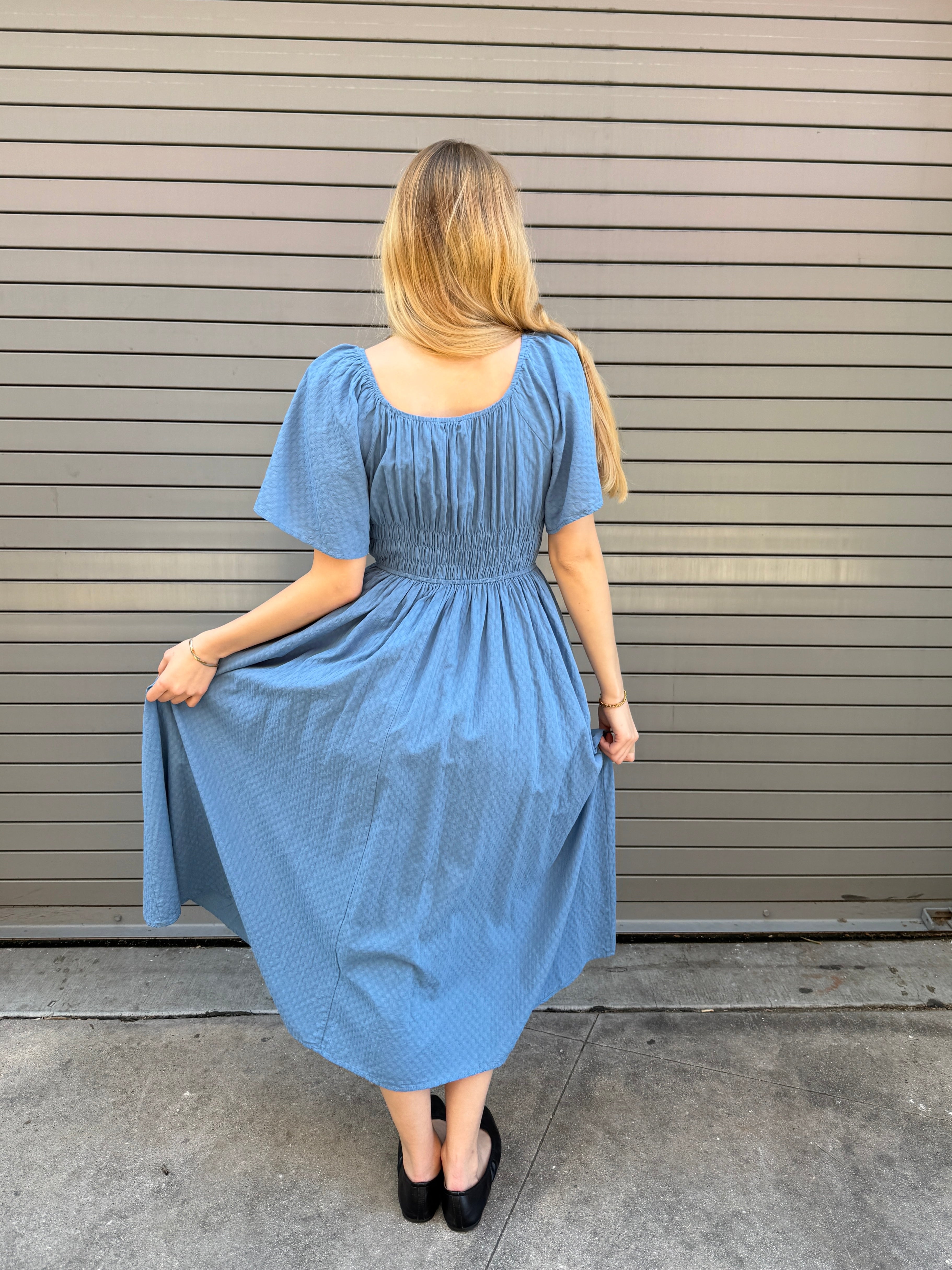 Woman wearing a blue dress standing against a metallic garage door.