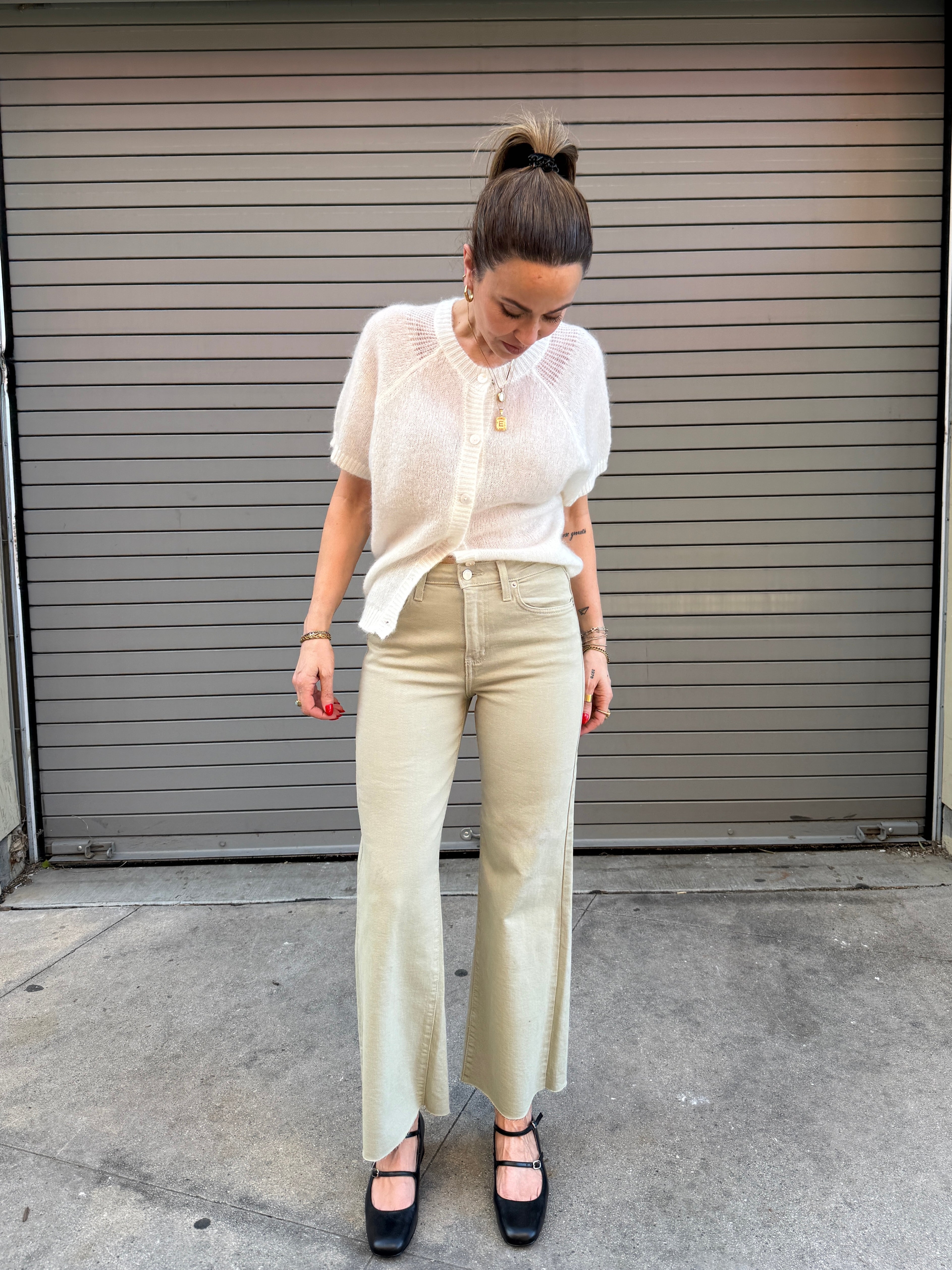 Woman wearing a white blouse and beige pants standing in front of a gray garage door.