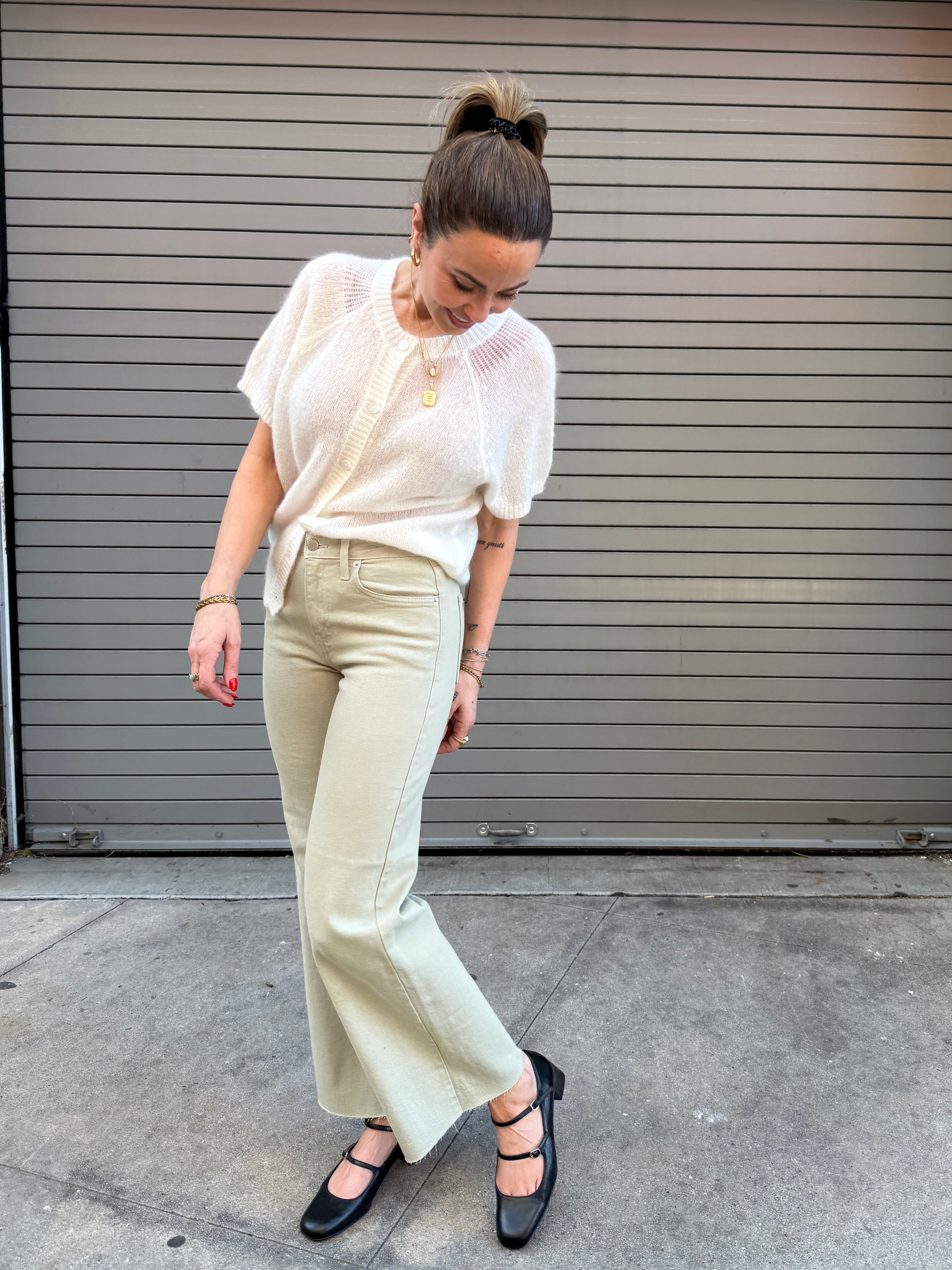 Woman in a white blouse and beige pants standing in front of a gray shutter.