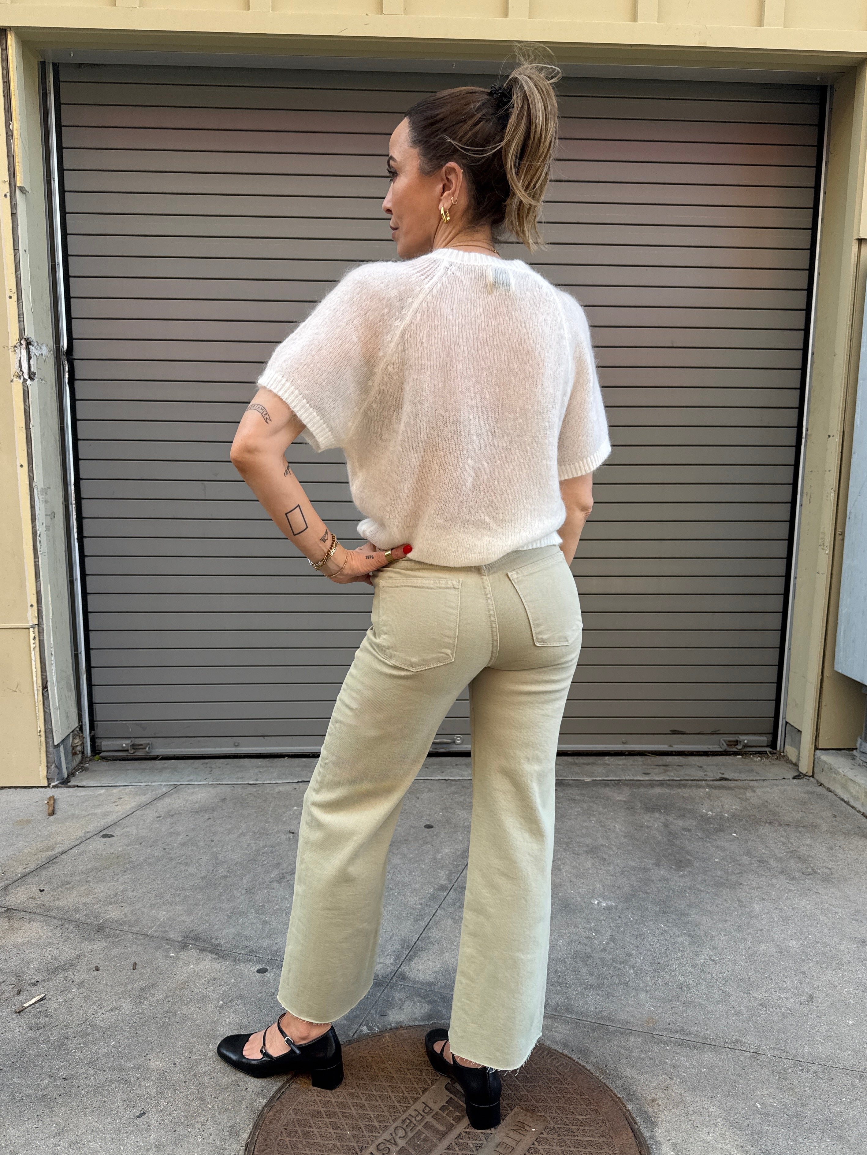 Woman wearing a white top and beige pants standing in front of a closed garage door.