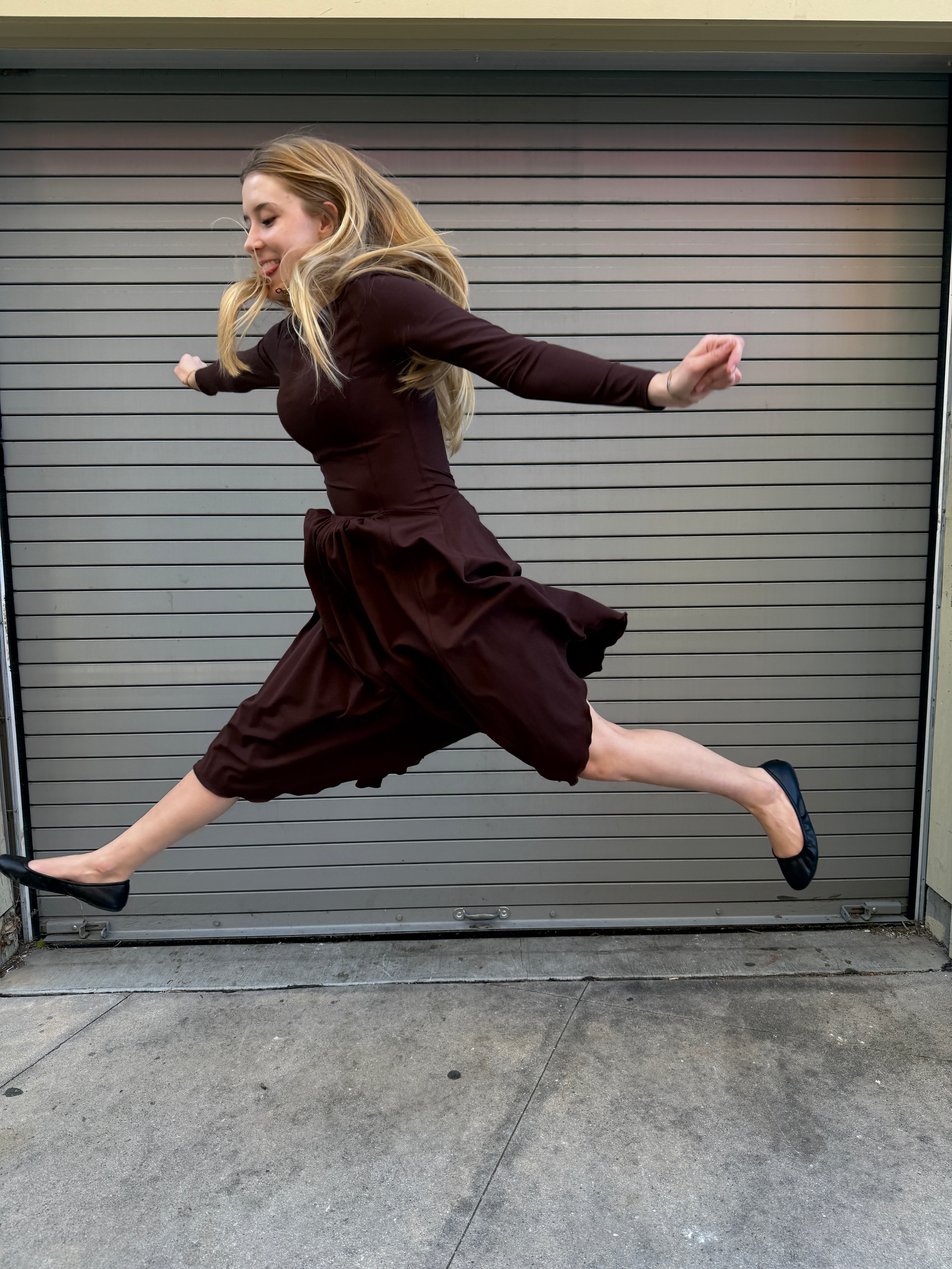 Person in a brown dress jumping up in front of a metal gate.