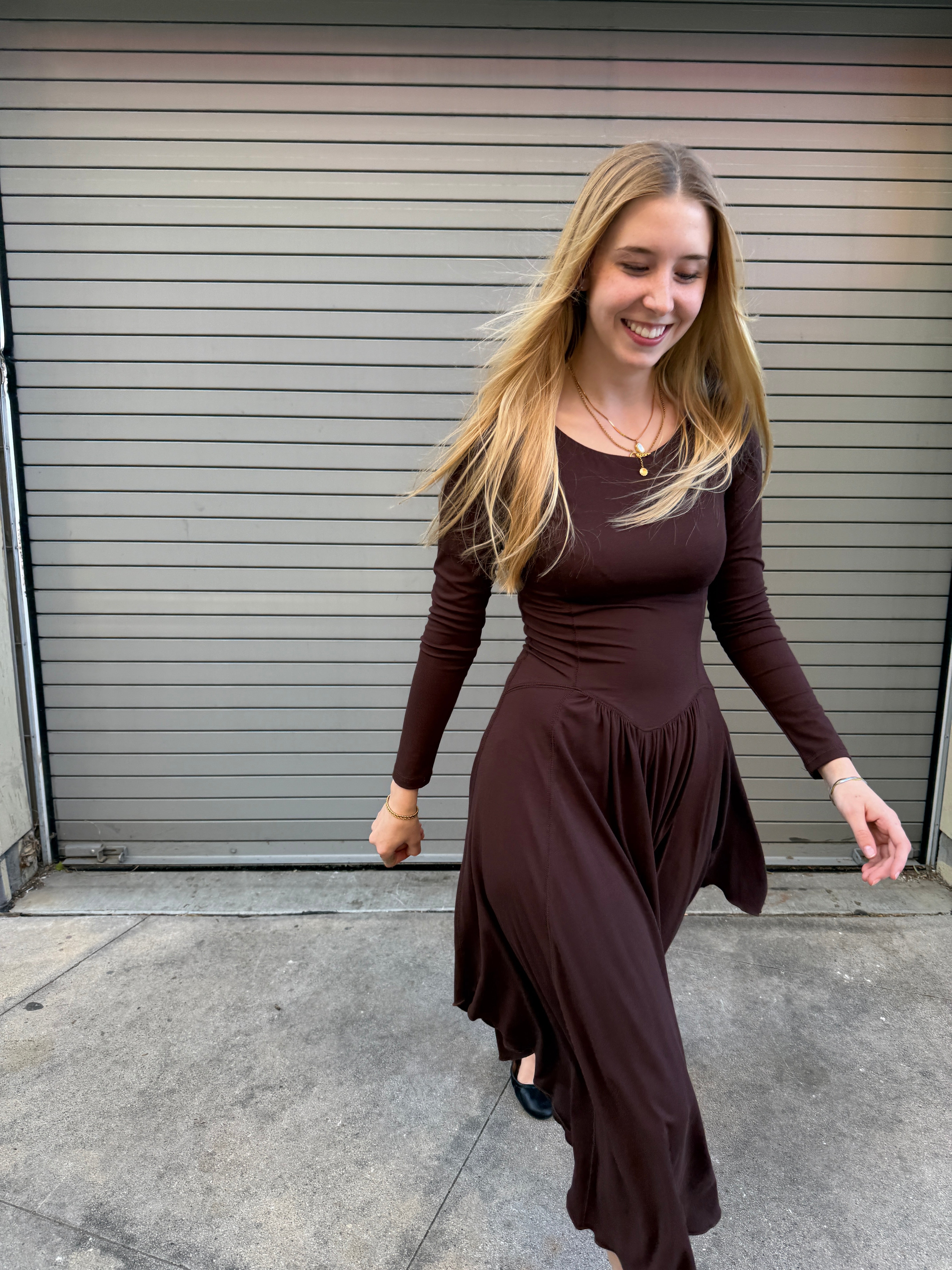 Woman in a brown dress standing on a sidewalk next to a metal gate.