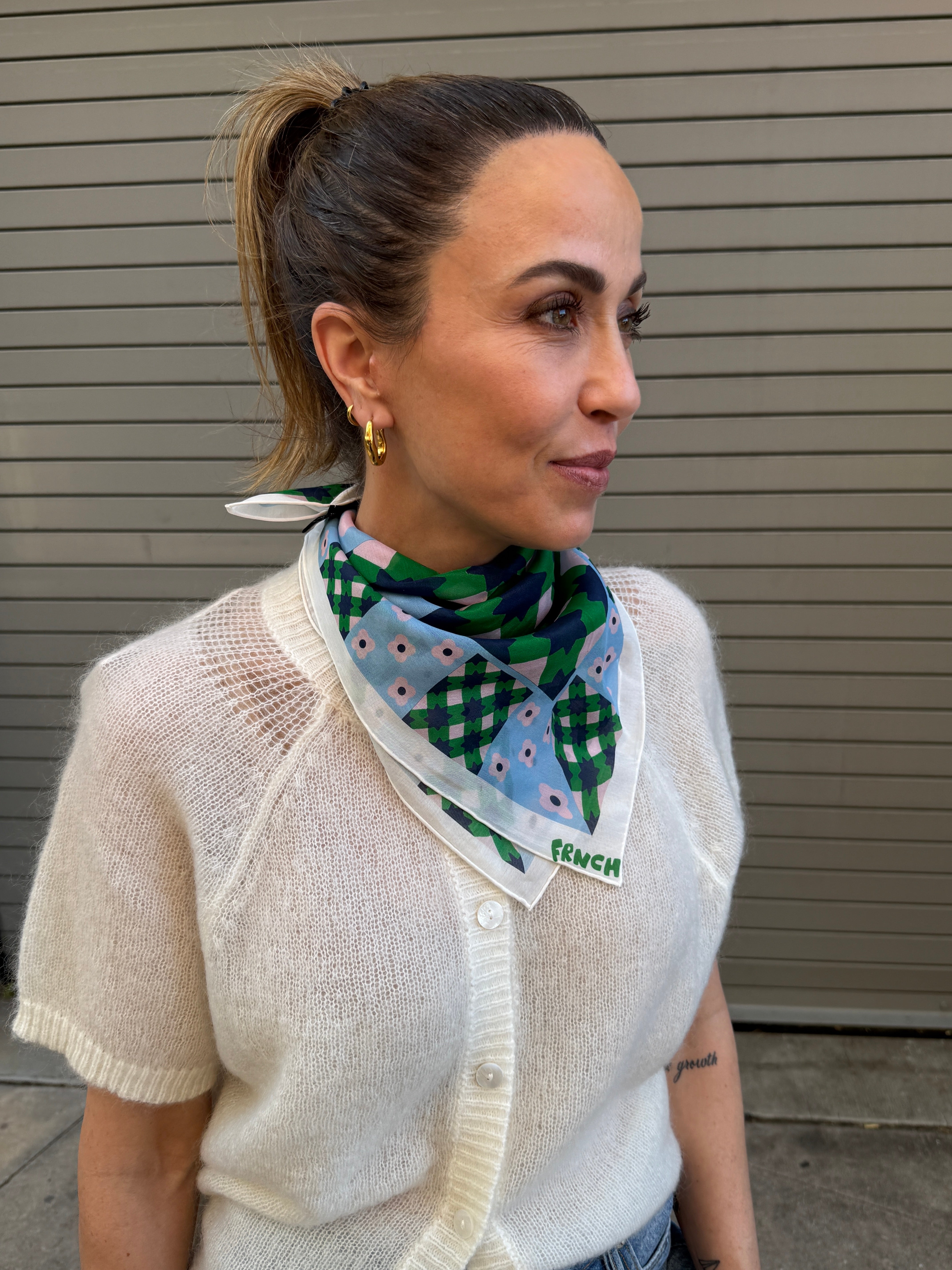 Woman wearing a patterned scarf with a visible brand logo against a neutral background