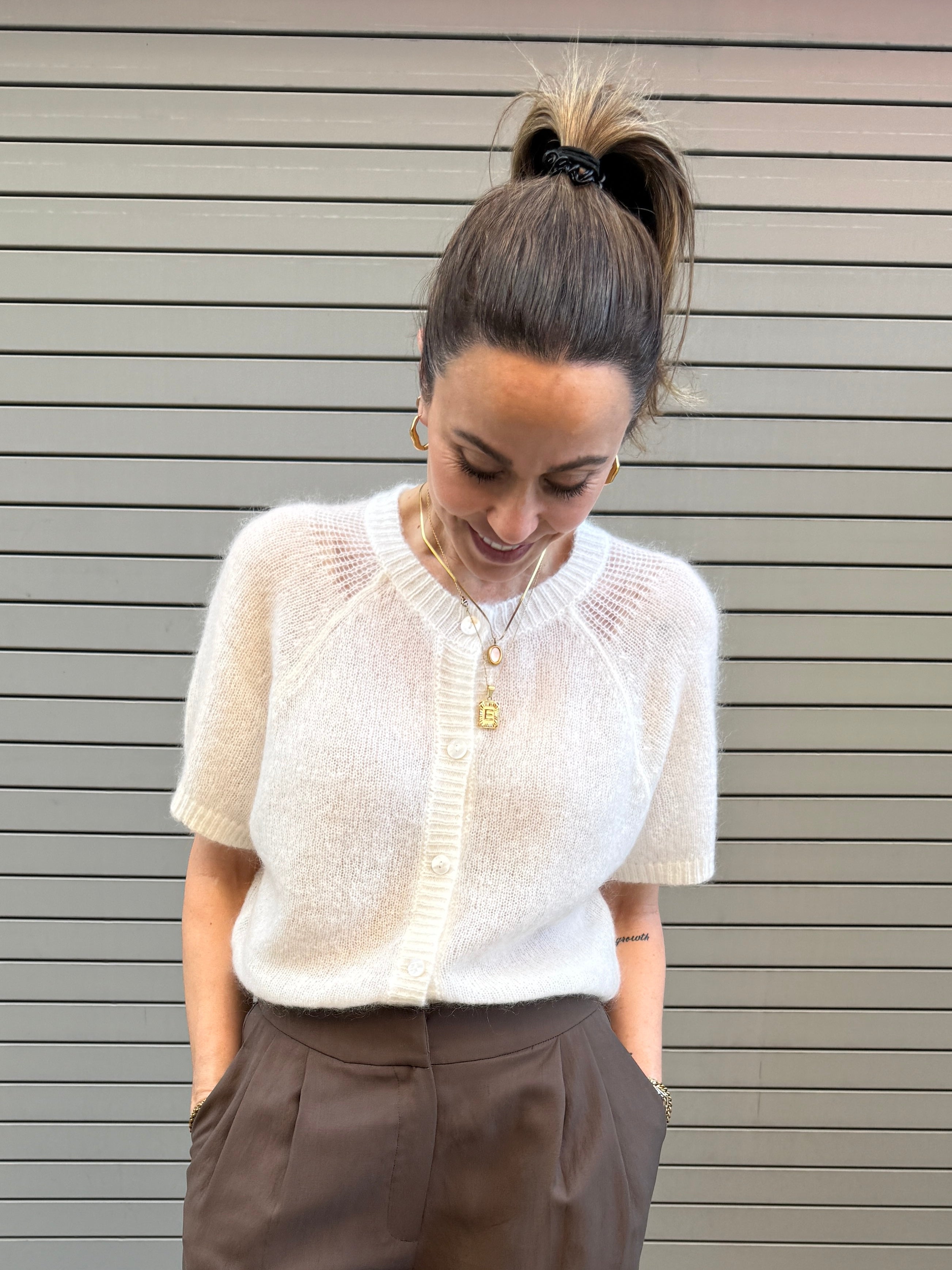 Woman wearing a white blouse and brown pants against a gray wall