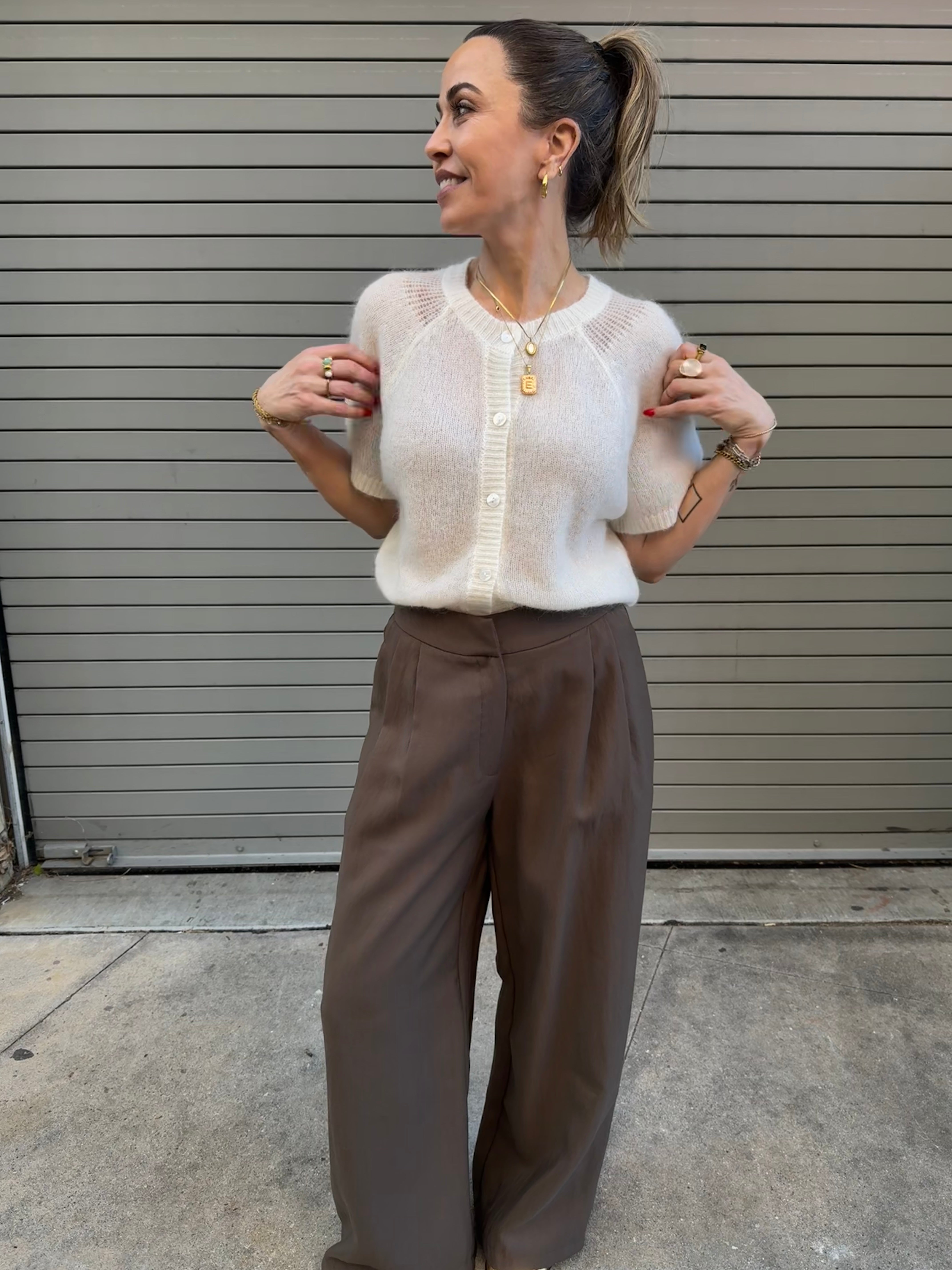 Woman wearing a white blouse and brown pants standing against a metallic shutter.
