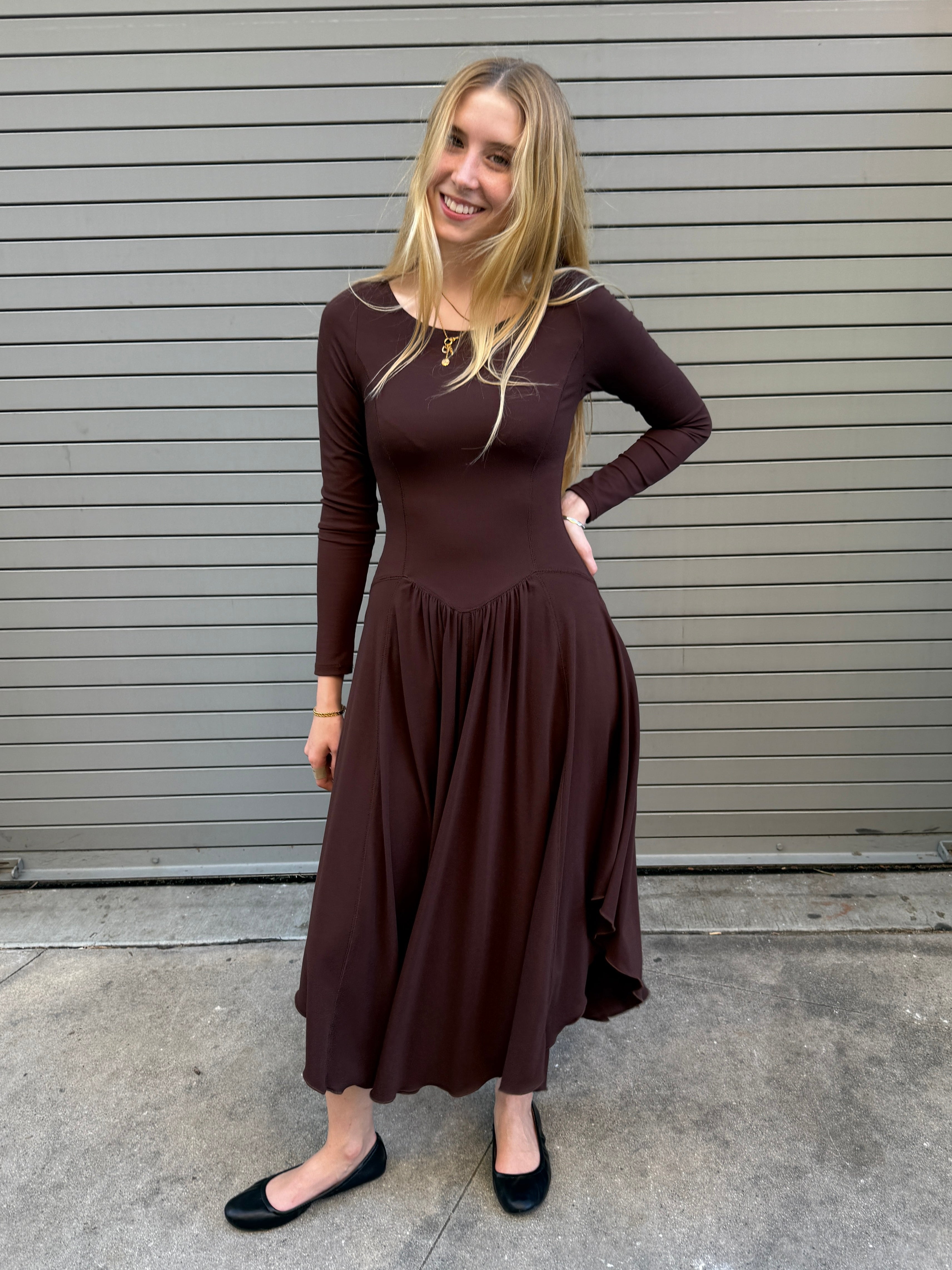 Woman wearing a brown dress standing in front of a gray wall.
