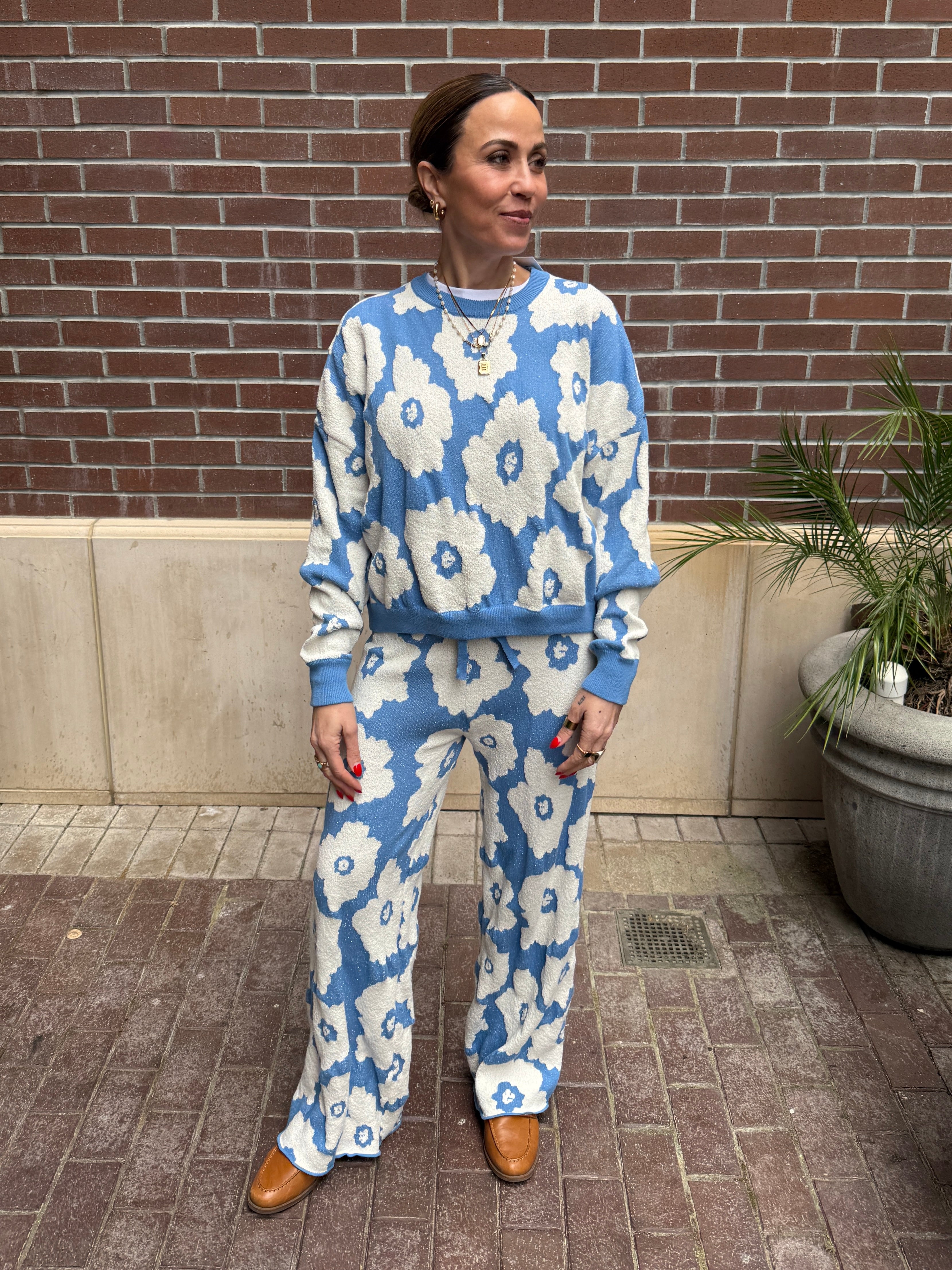 Woman wearing a blue and white floral outfit standing against a brick wall.