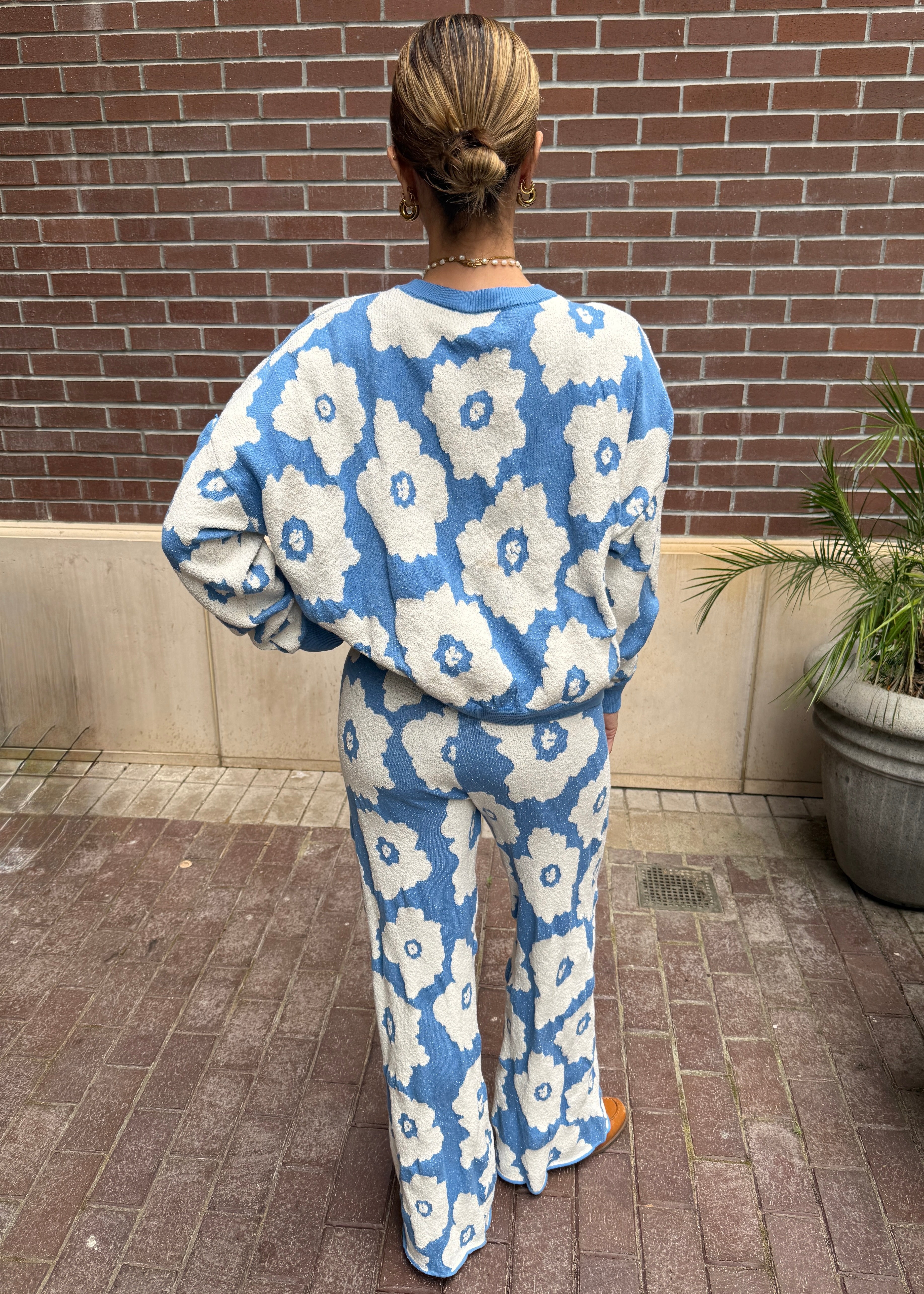 Person wearing a blue and white floral patterned outfit standing against a brick wall.