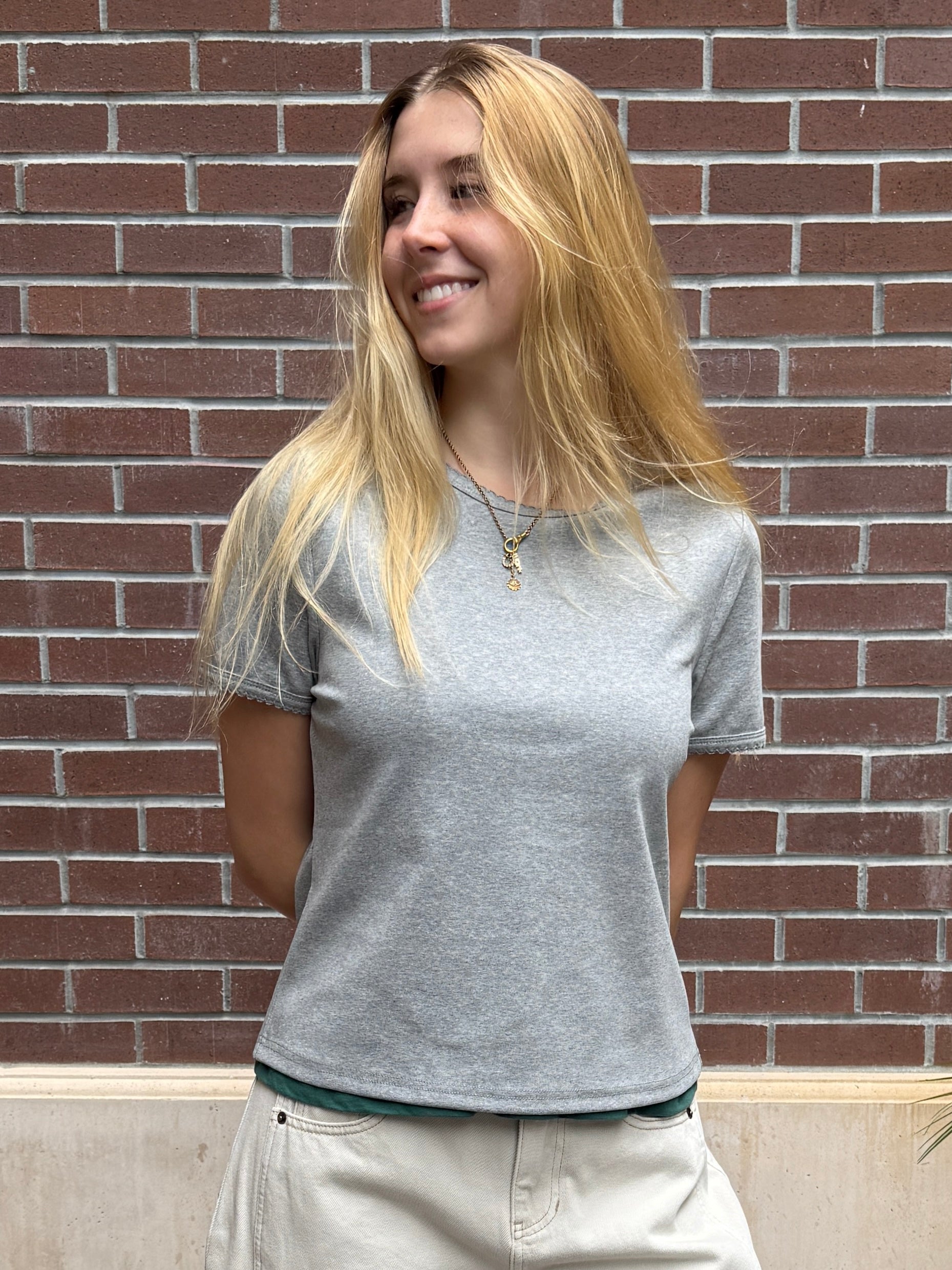 Woman wearing a gray t-shirt standing in front of a brick wall