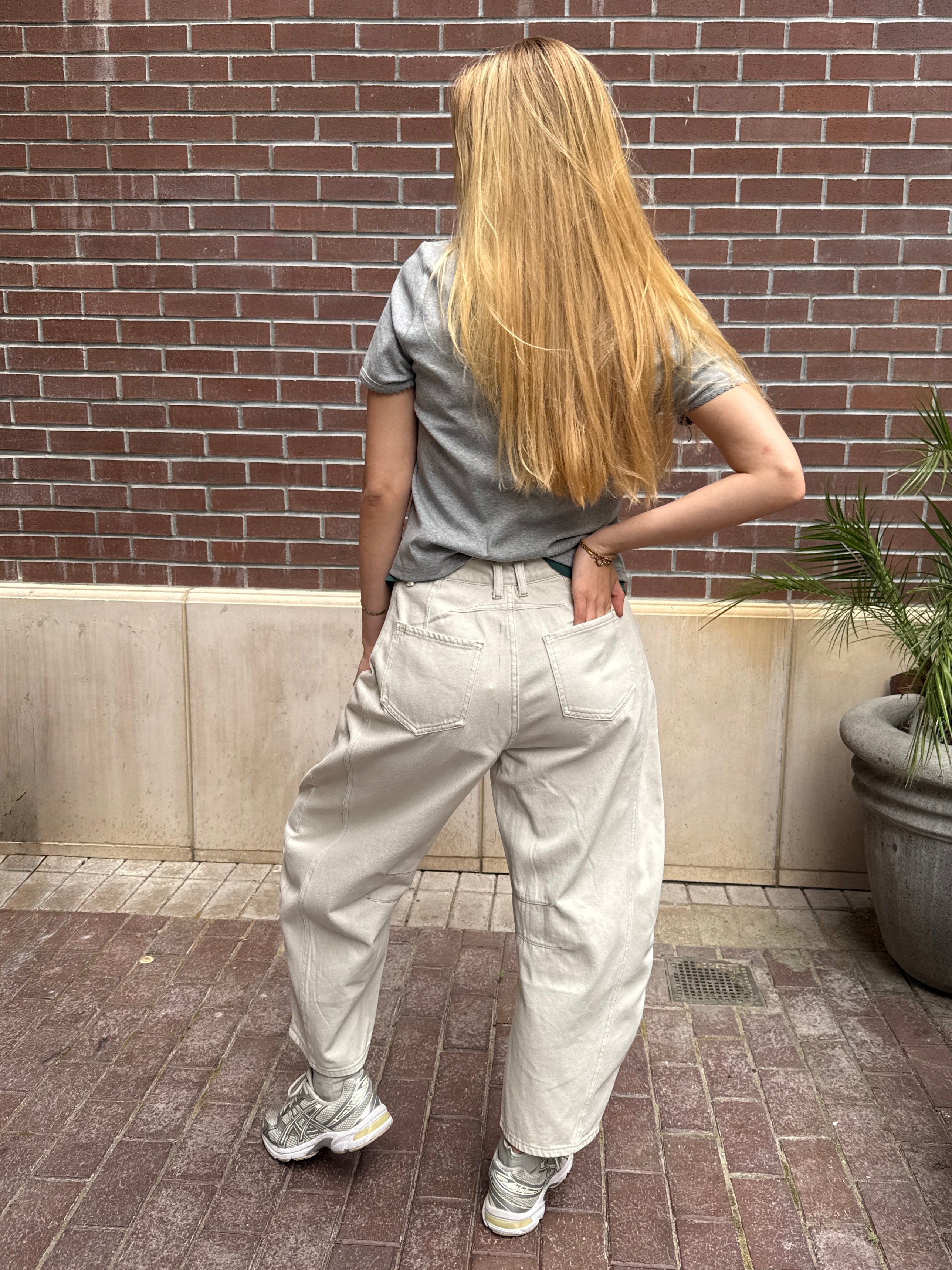Person wearing a gray shirt and light-colored pants standing against a brick wall.