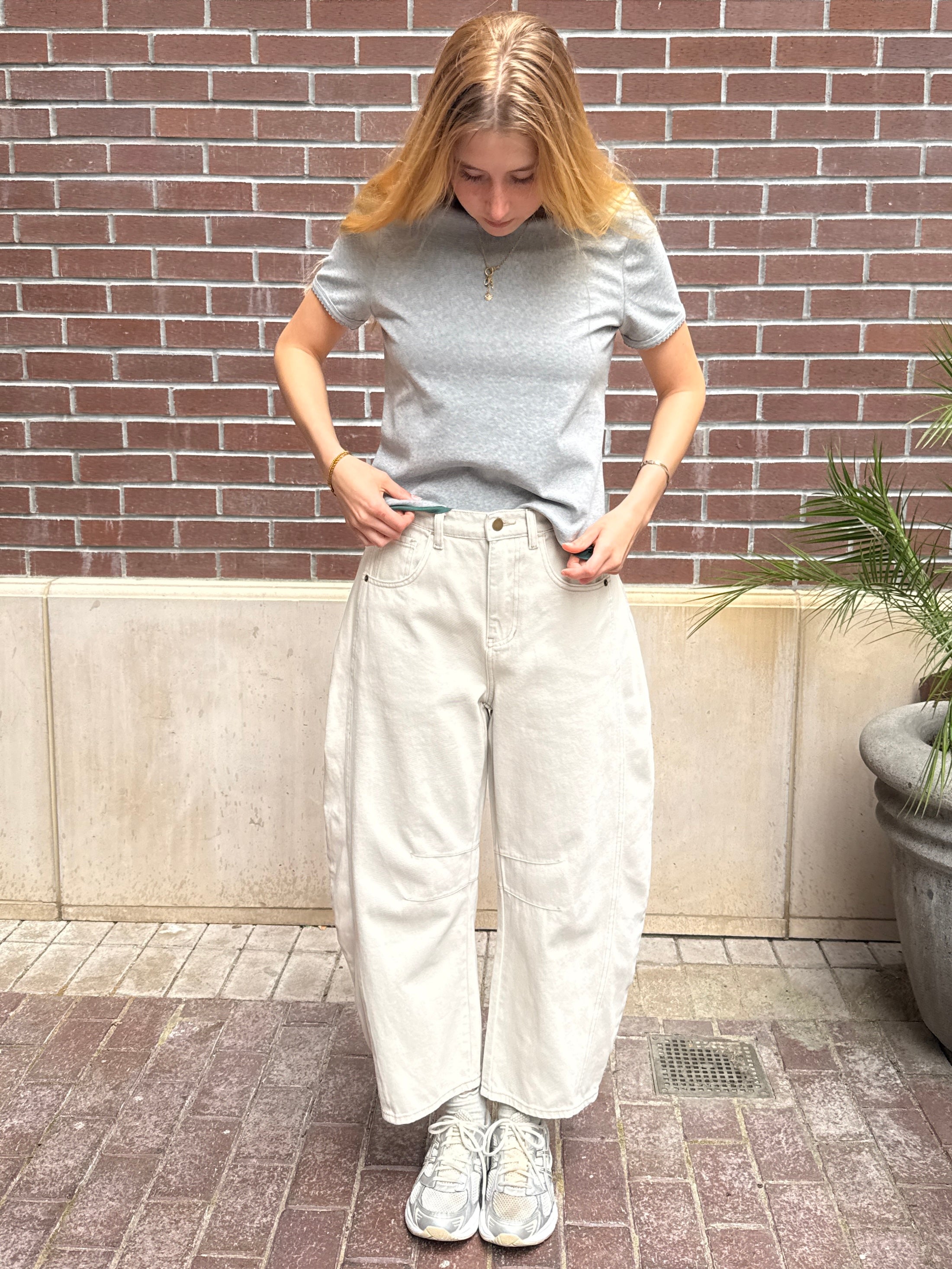 Person wearing a gray t-shirt and white pants standing against a brick wall.