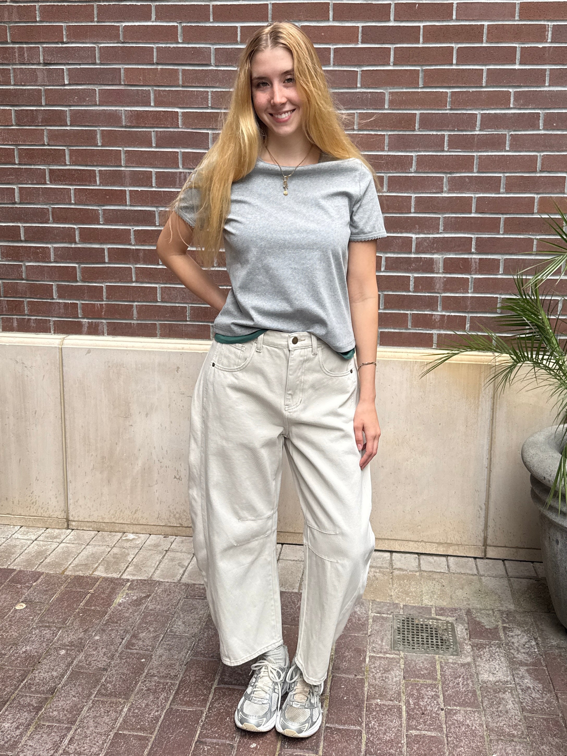 Person wearing a gray t-shirt and white pants standing against a brick wall.