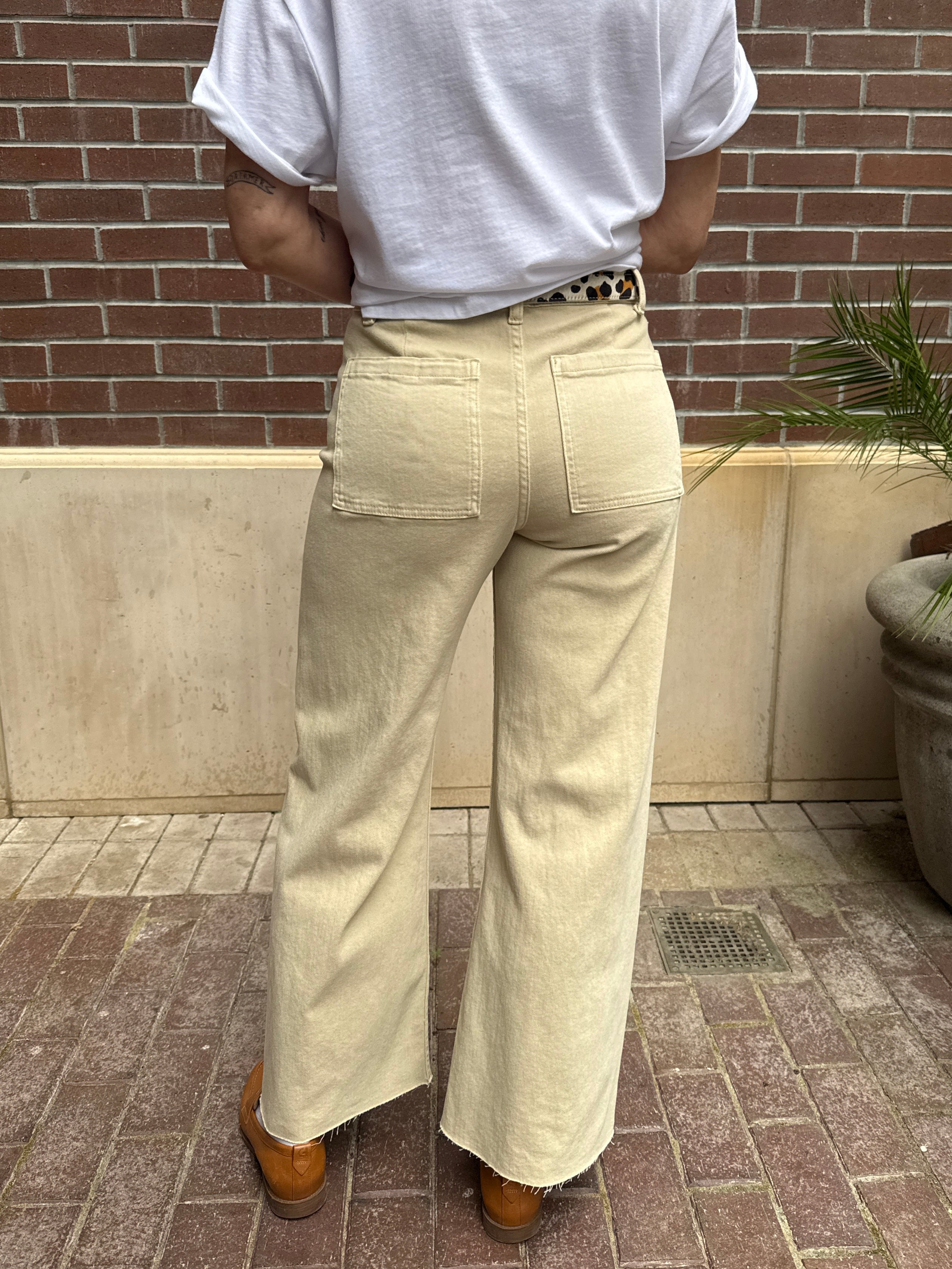 Person wearing beige wide-leg pants and a white shirt against a brick wall.