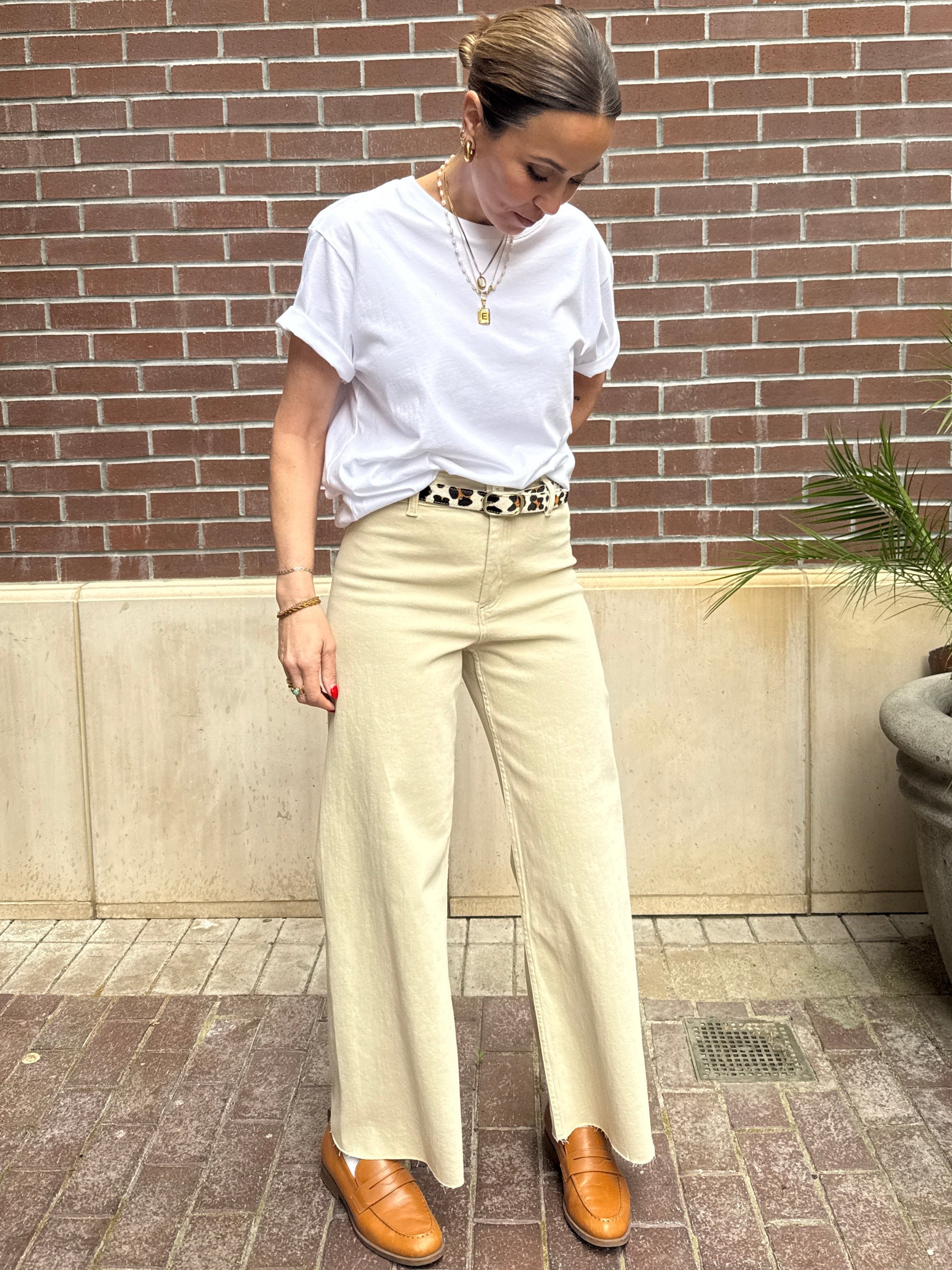 Person wearing a white t-shirt, beige pants, and brown shoes against a brick wall.