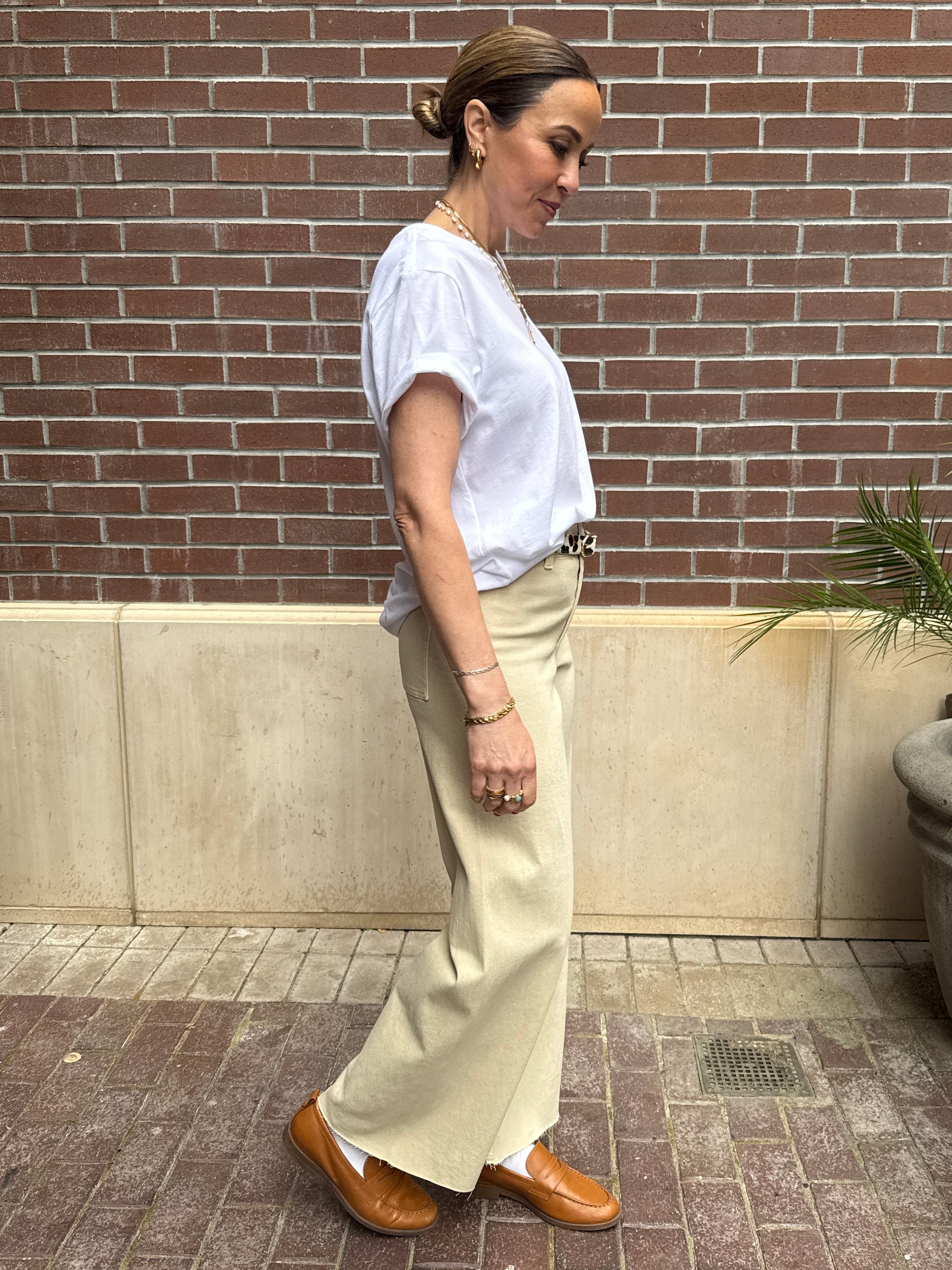 Woman in a white shirt and beige pants standing against a brick wall.