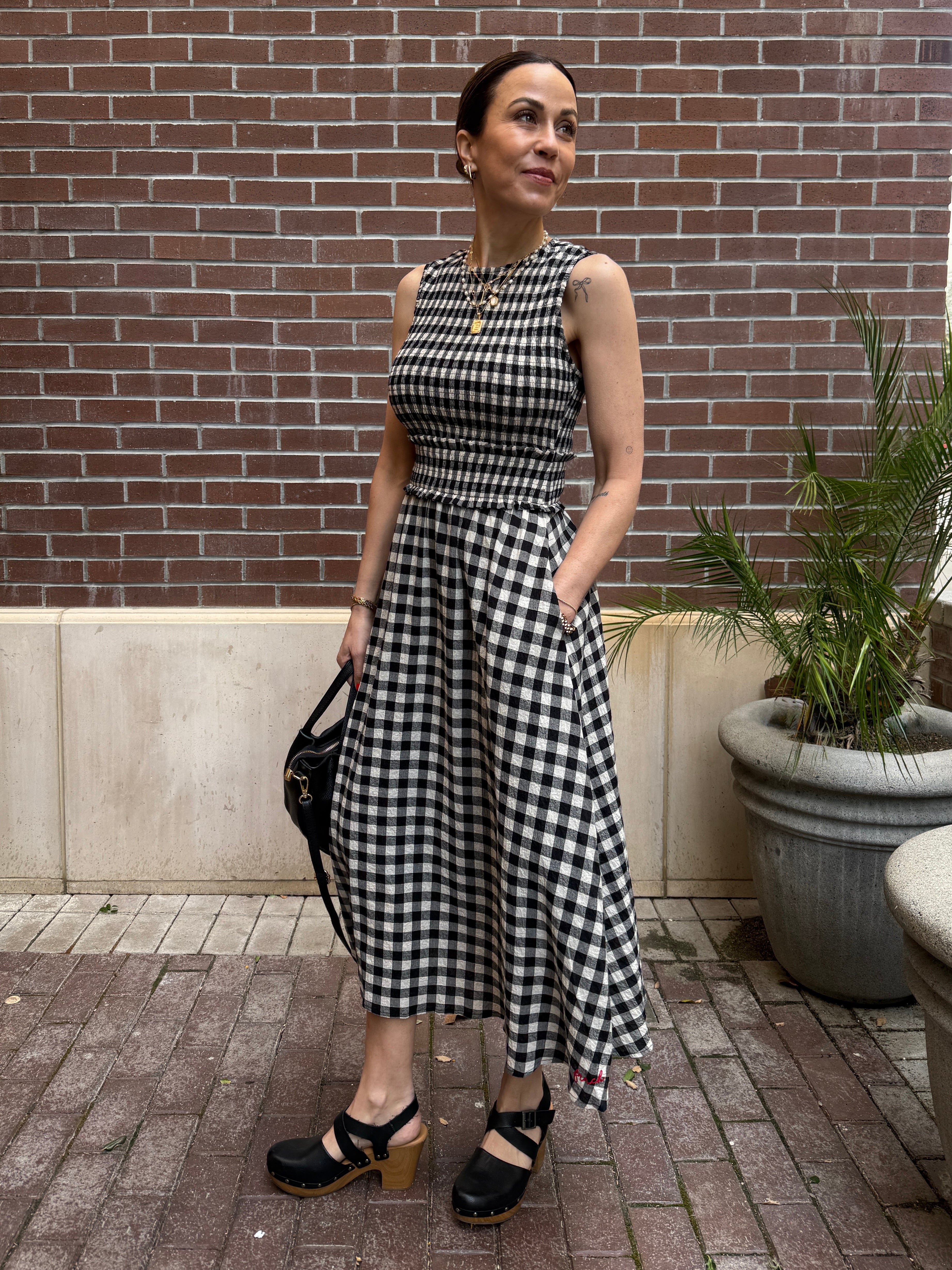 Woman in a black and white checkered dress standing against a brick wall.